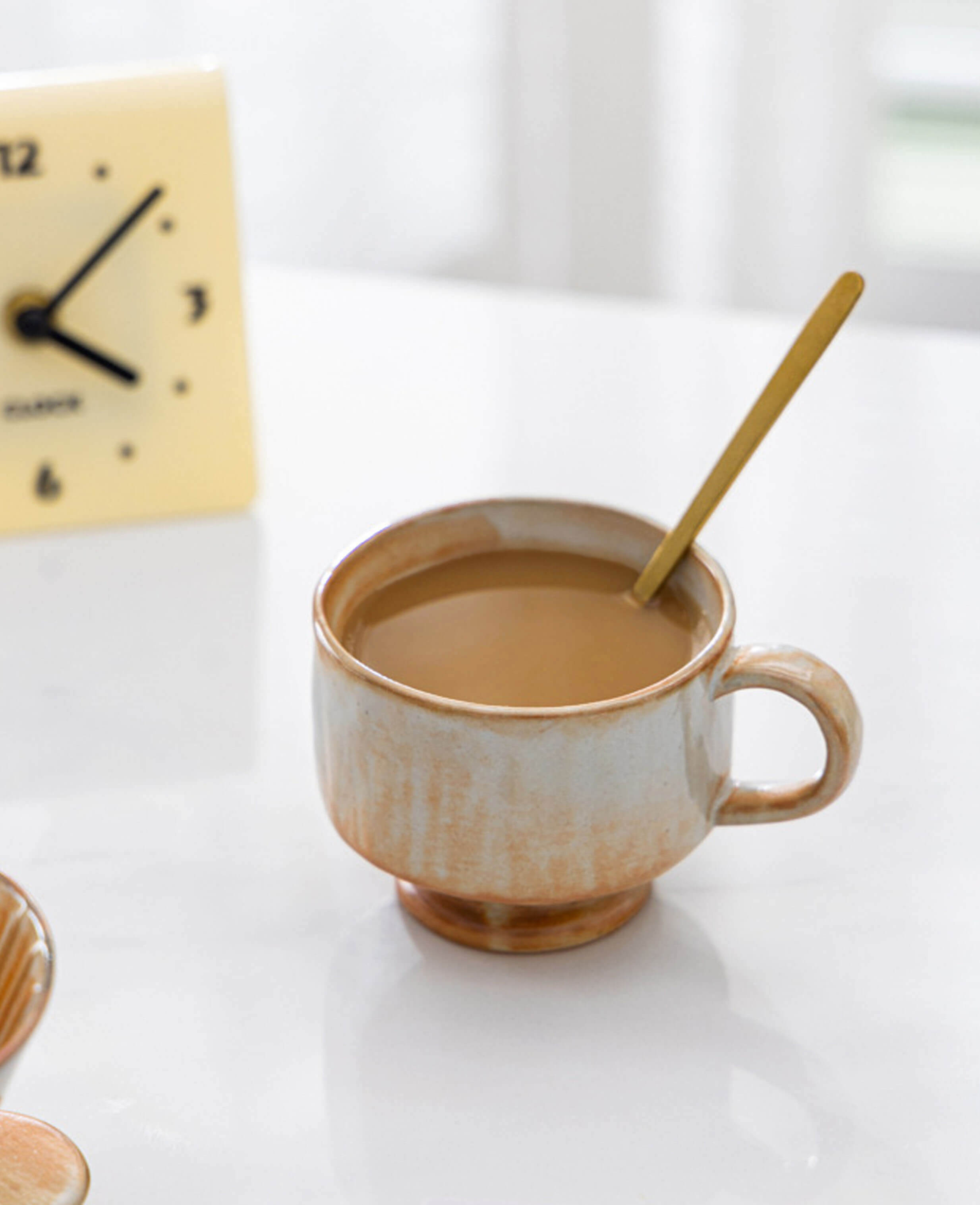 dawn chalice handcrafted ceramic coffee and tea cup filled with latte with warm earthy glaze on white table with gold spoon