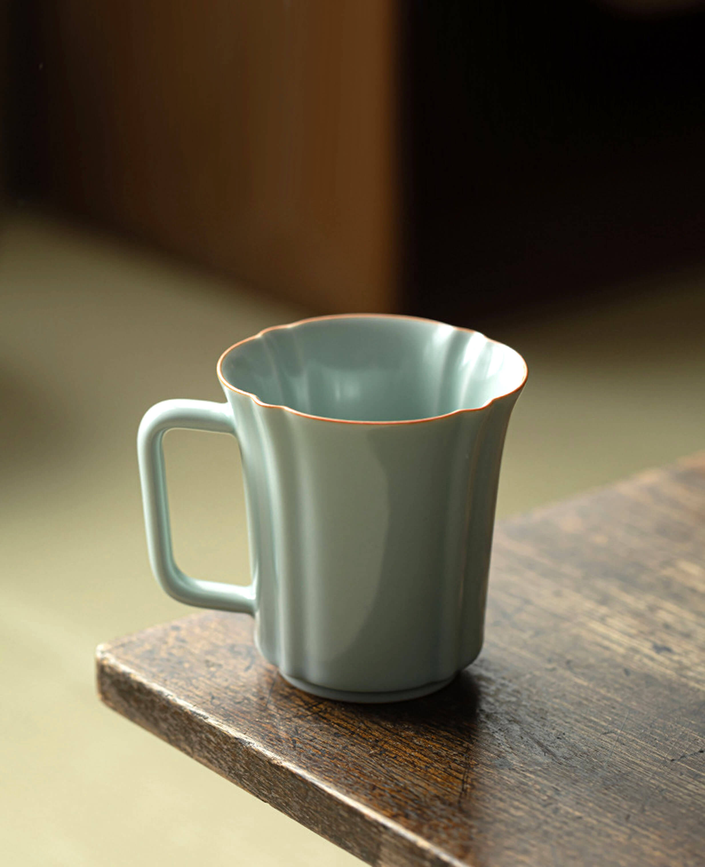 soft celadon green porcelain mug echo of ru with scalloped rim sitting on edge of table