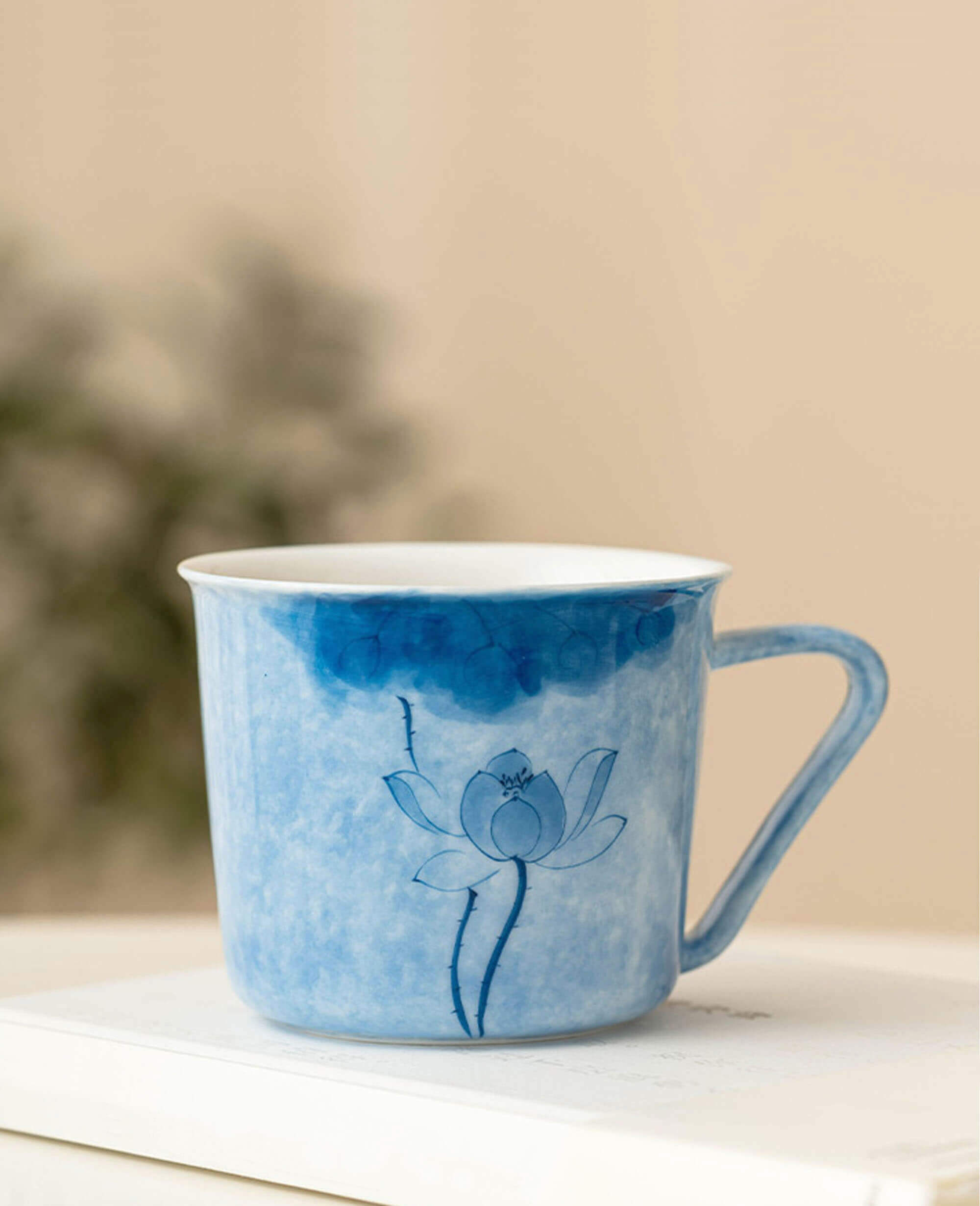 inked drizzle hand painted coffee and tea cup with blue lotus sitting on book in warm natural light
