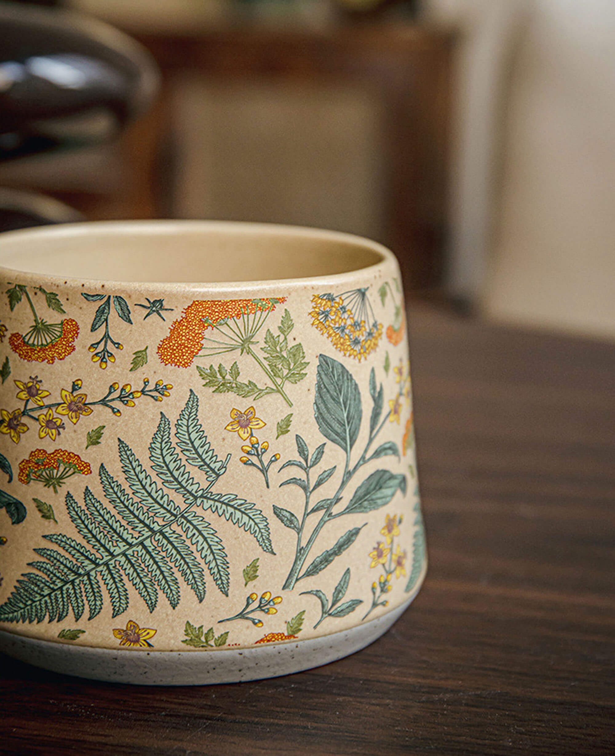 close up of july note ceramic mug with wildflower and fern pattern on a wooden table highlighting glaze texture