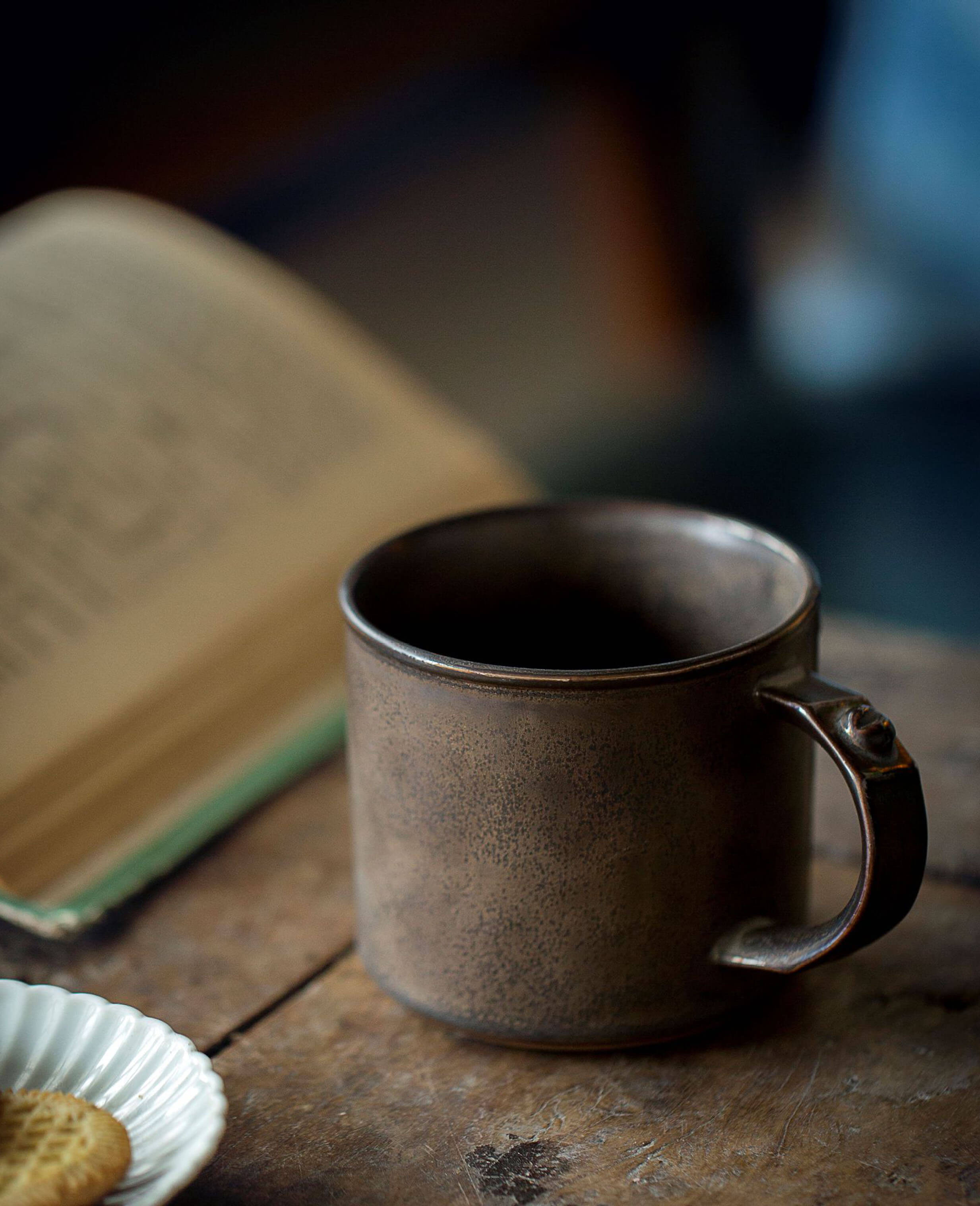 handmade ironhold mug next to an open book and biscuits