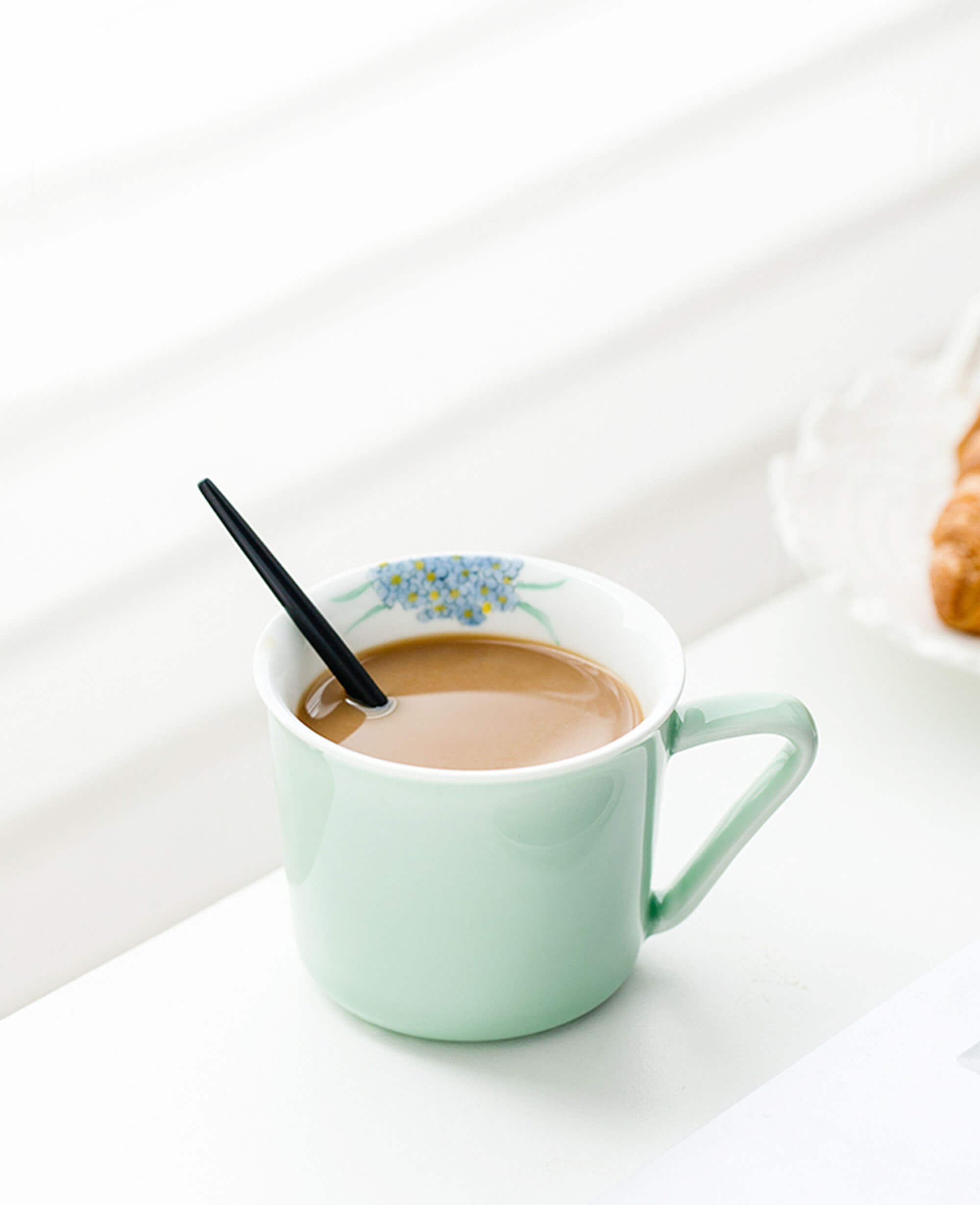 minted memory hand painted floral porcelain coffee and tea cup filled with coffee on a white tabletop
