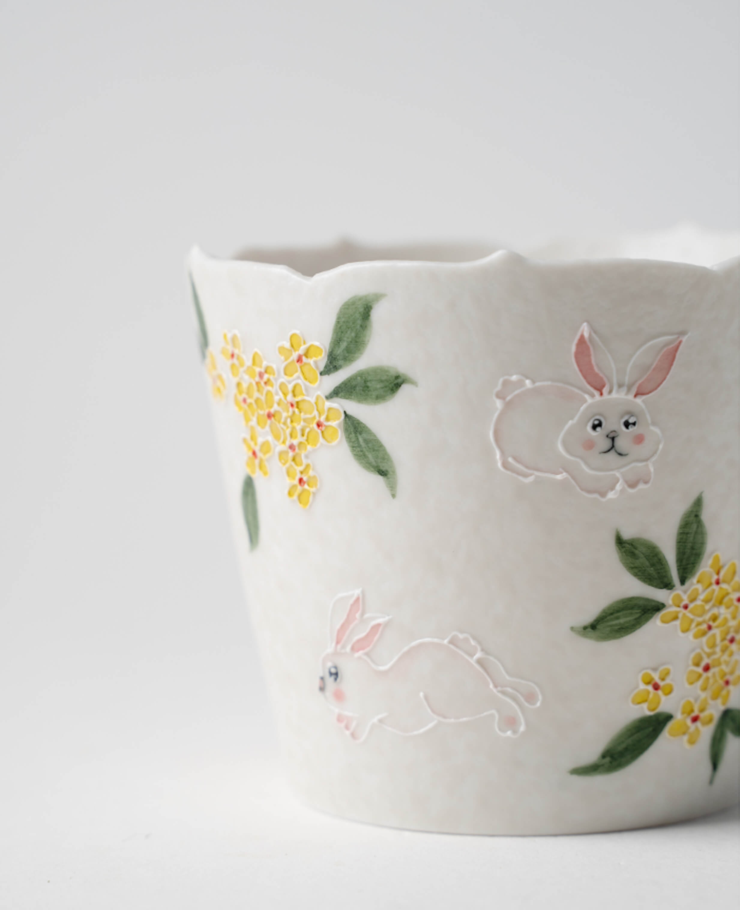 close up of nectar hop hand painted ceramic cup showing rabbit leaping among golden osmanthus blossoms