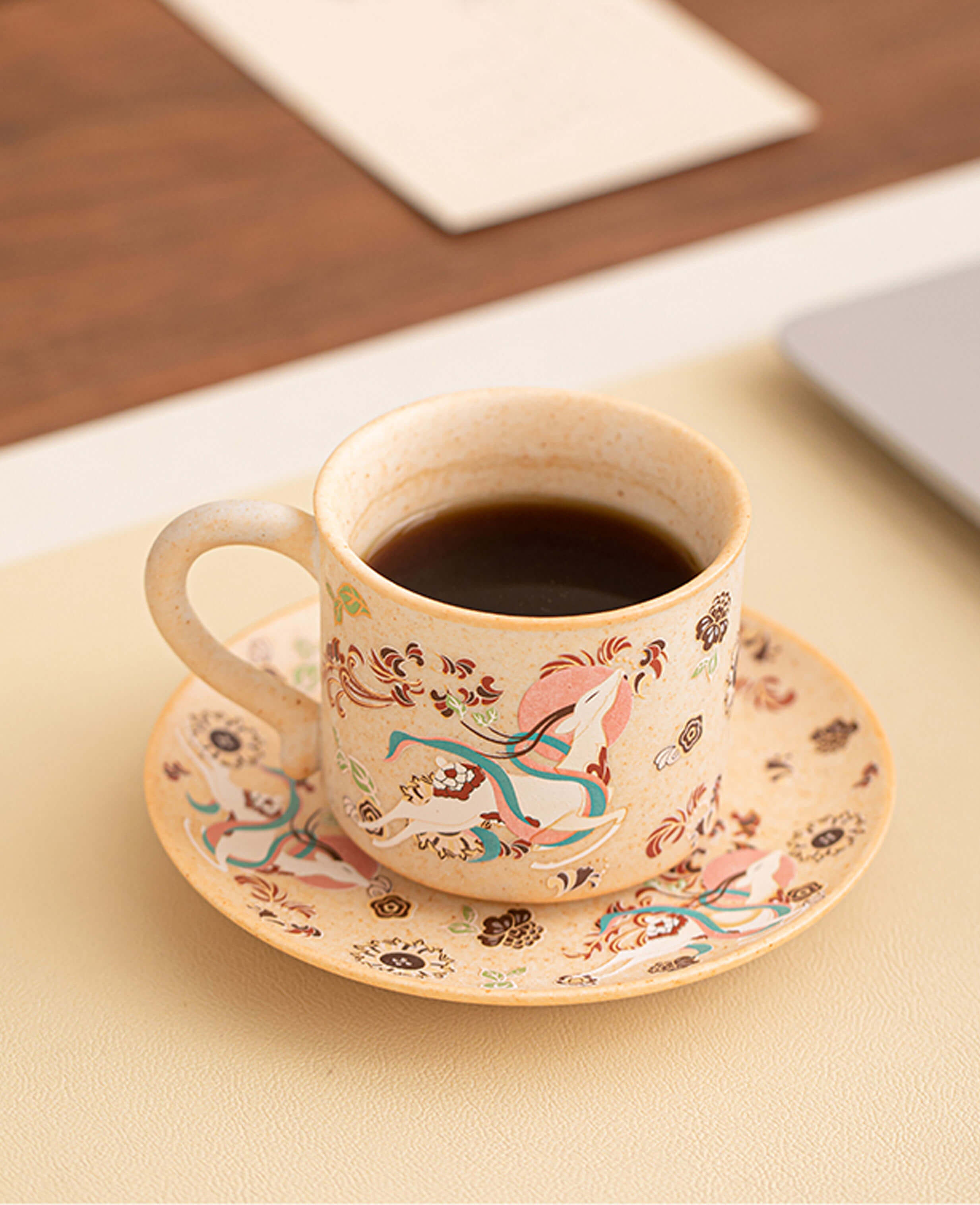 nine coloured deer ceramic cup filled with black coffee on matching dunhuang motif saucer