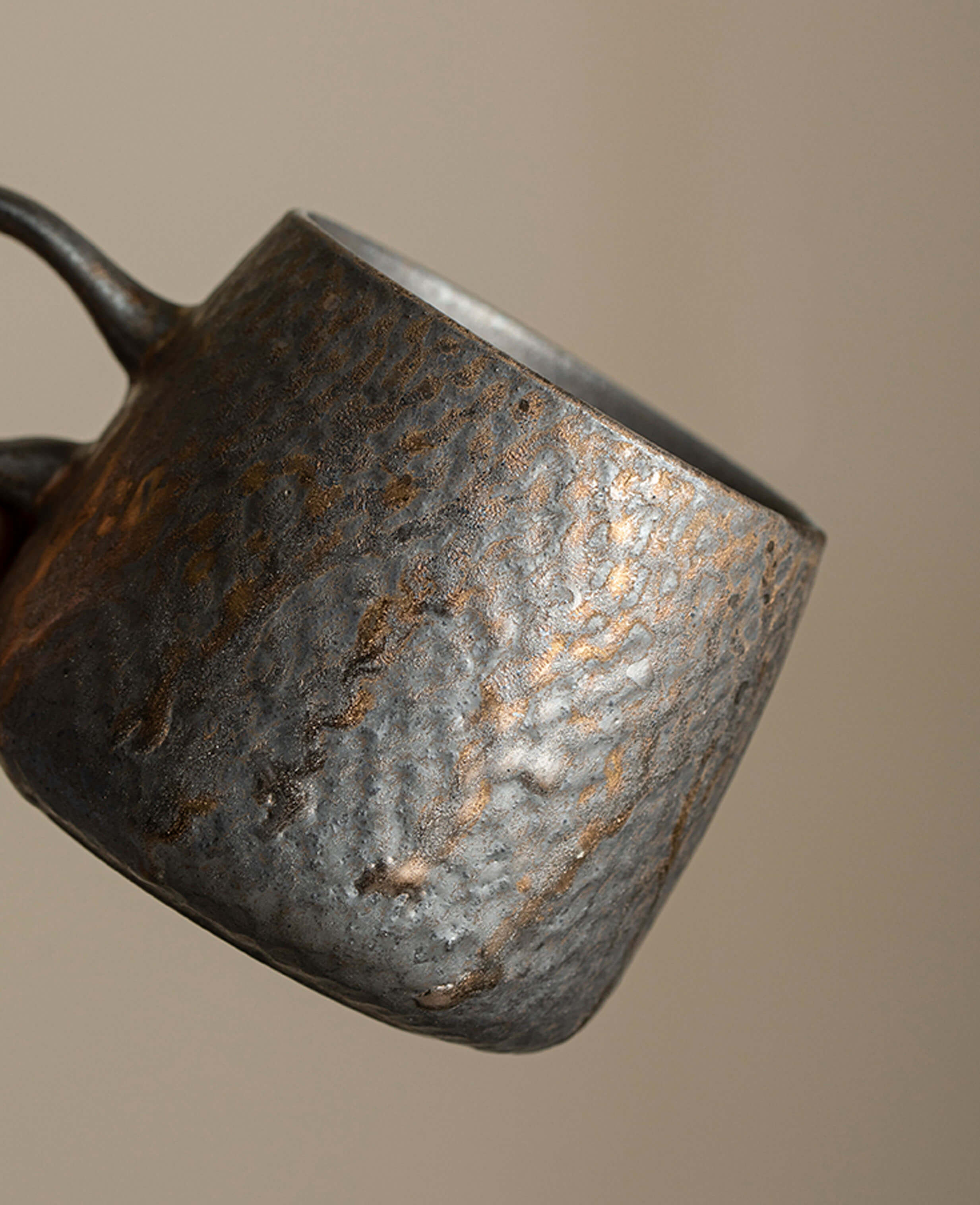 a close-up view of the coffee cup surface showing the flowing, ripple-like texture and golden rustic hues of the handcrafted glaze