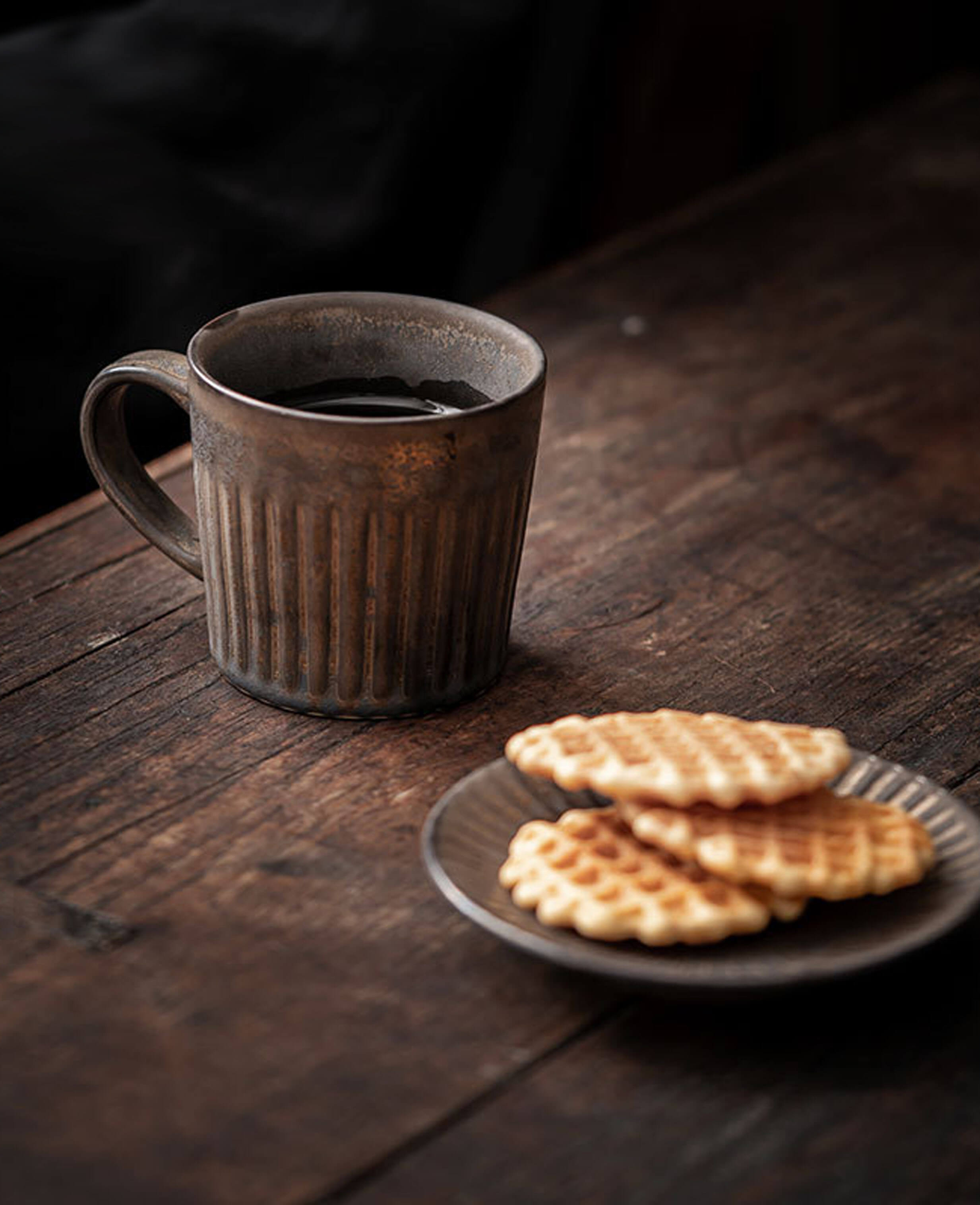 front view of rustglow strata textured stoneware coffee cup with subtle golden tones resting on a rustic wooden table
