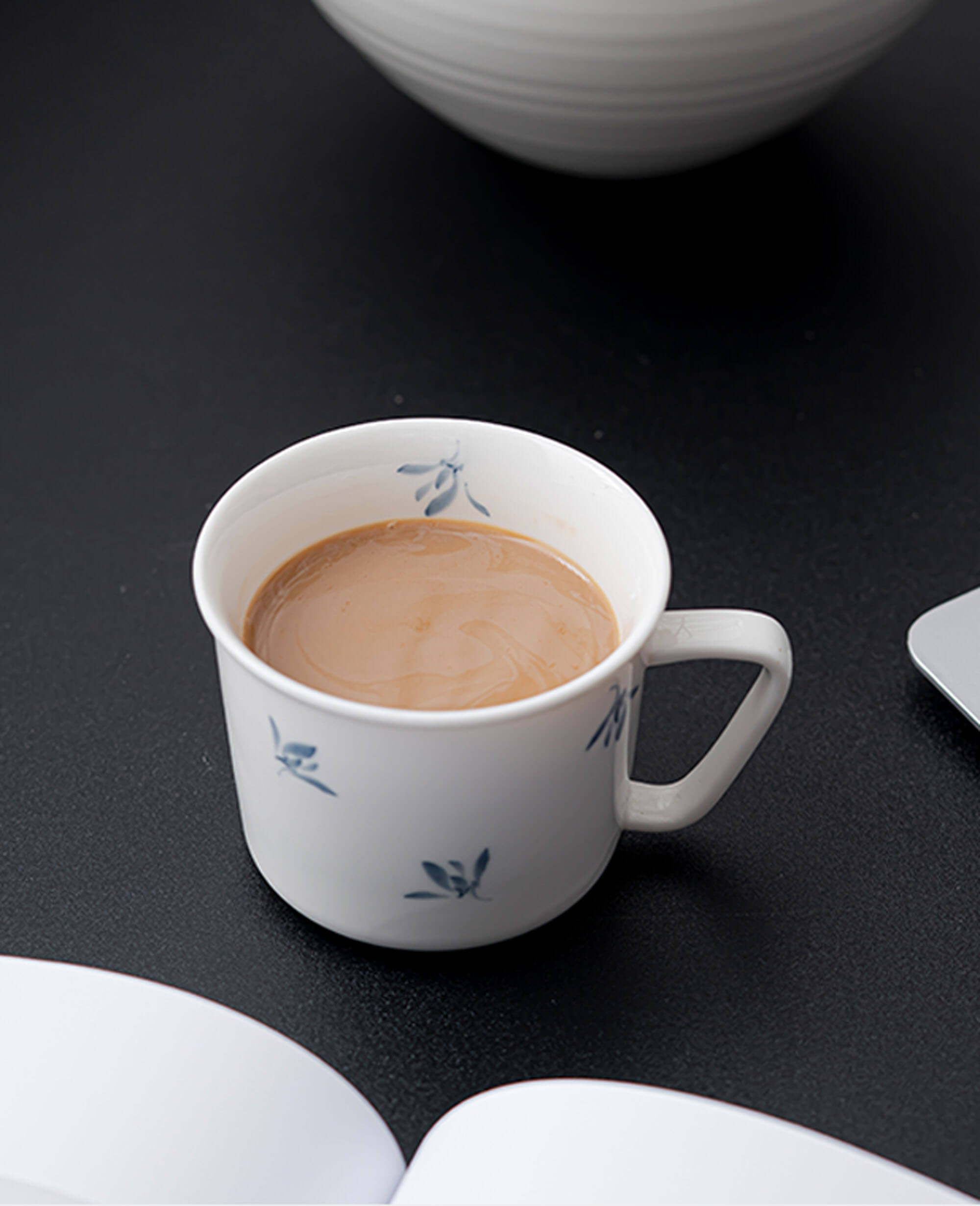 porcelain coffee and tea cup with soft blue leaf motif on black desk beside an open book from the serene drift painted diary collection