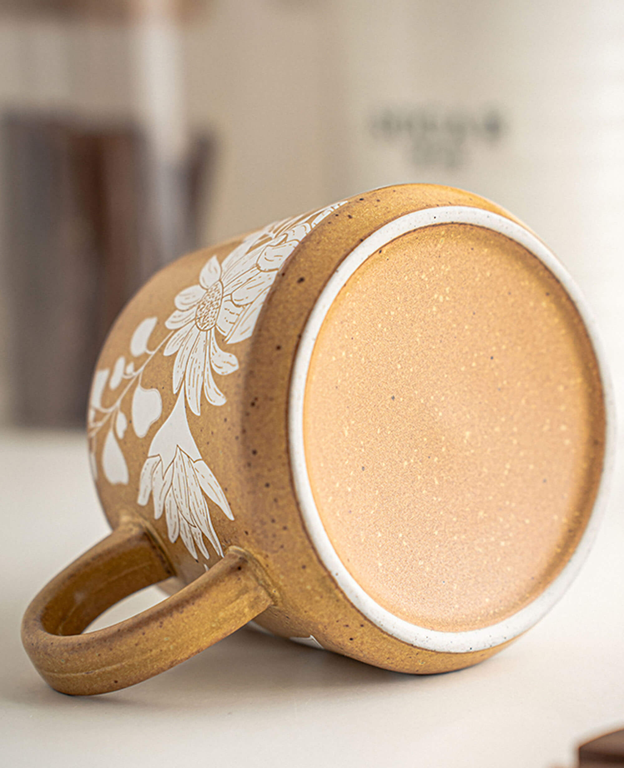 bottom view of artisan ceramic mug showing detailed floral carving and raw stoneware finish