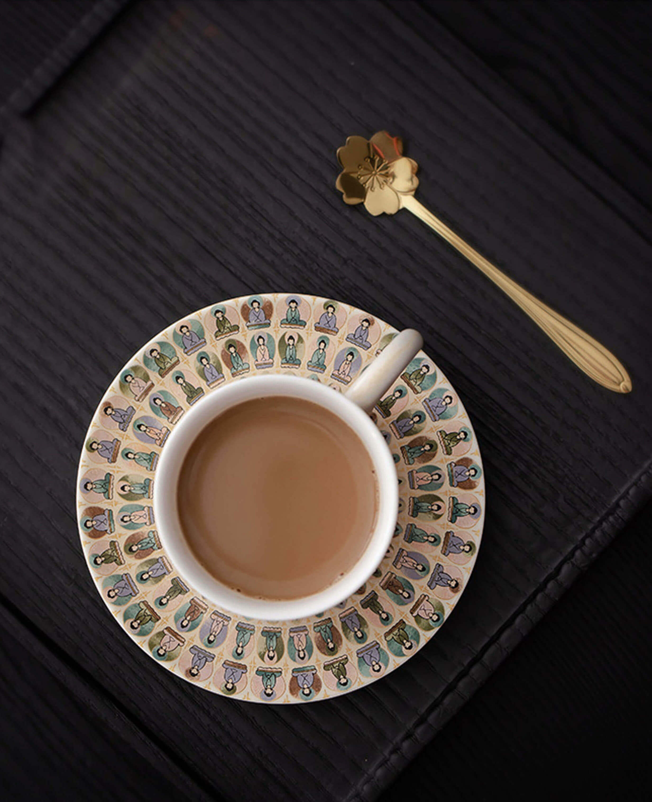 top view of handcrafted ceramic coffee cup and saucer with buddha motif and lotus shaped spoon on black table
