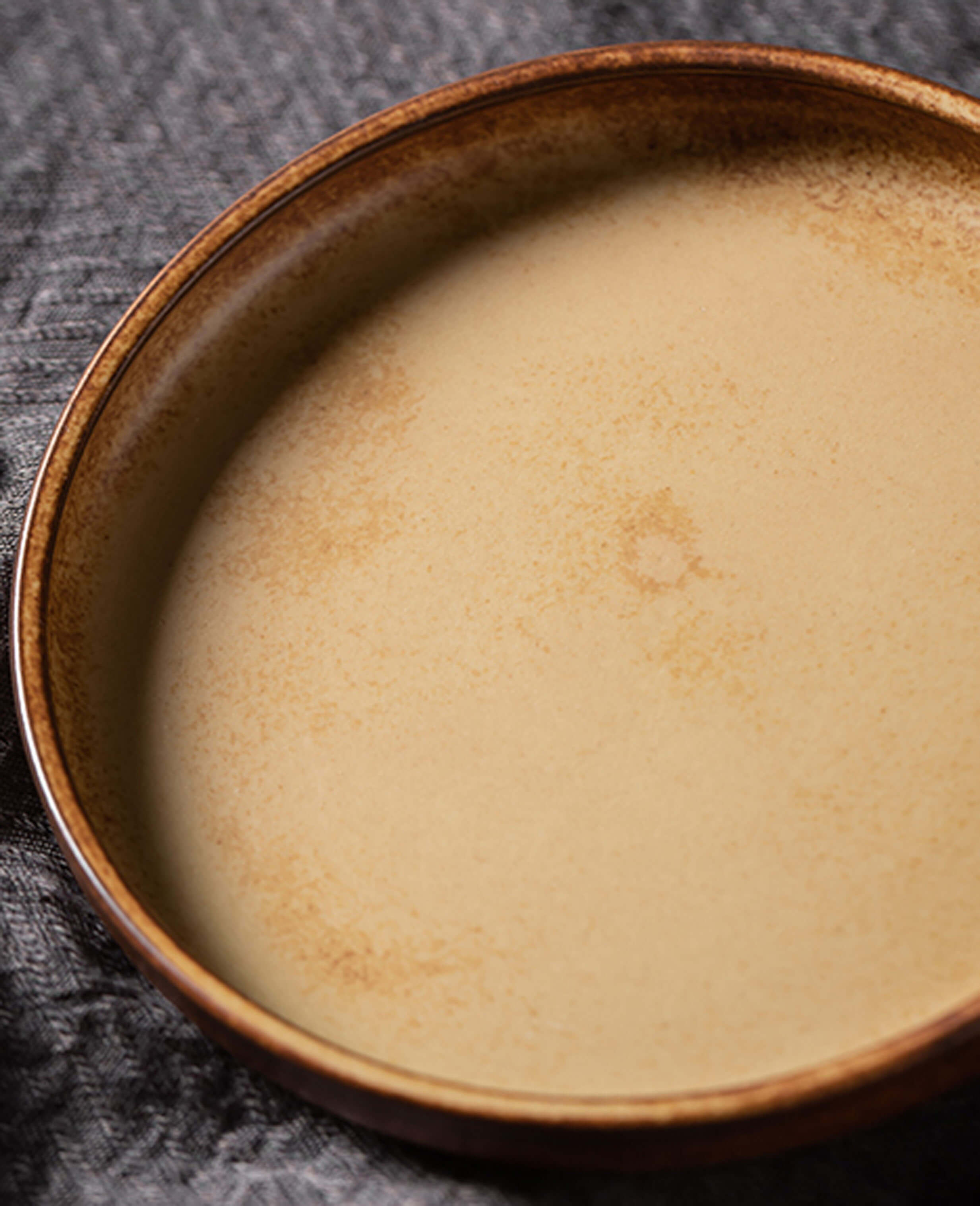 close up of toffee reverie bellara ceramic saucer with soft matte finish and warm golden tones