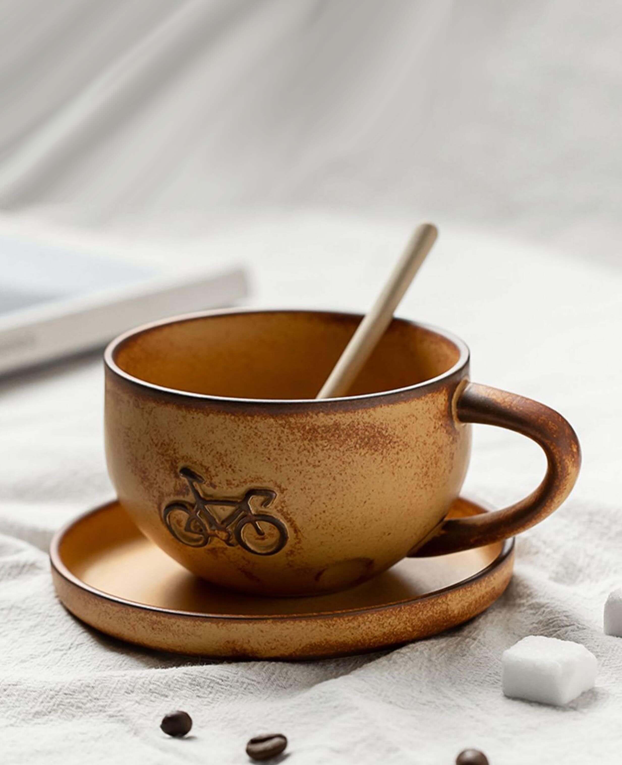 toffee reverie pedalstone bicycle embossed coffee mug on saucer with coffee spoon on cloth