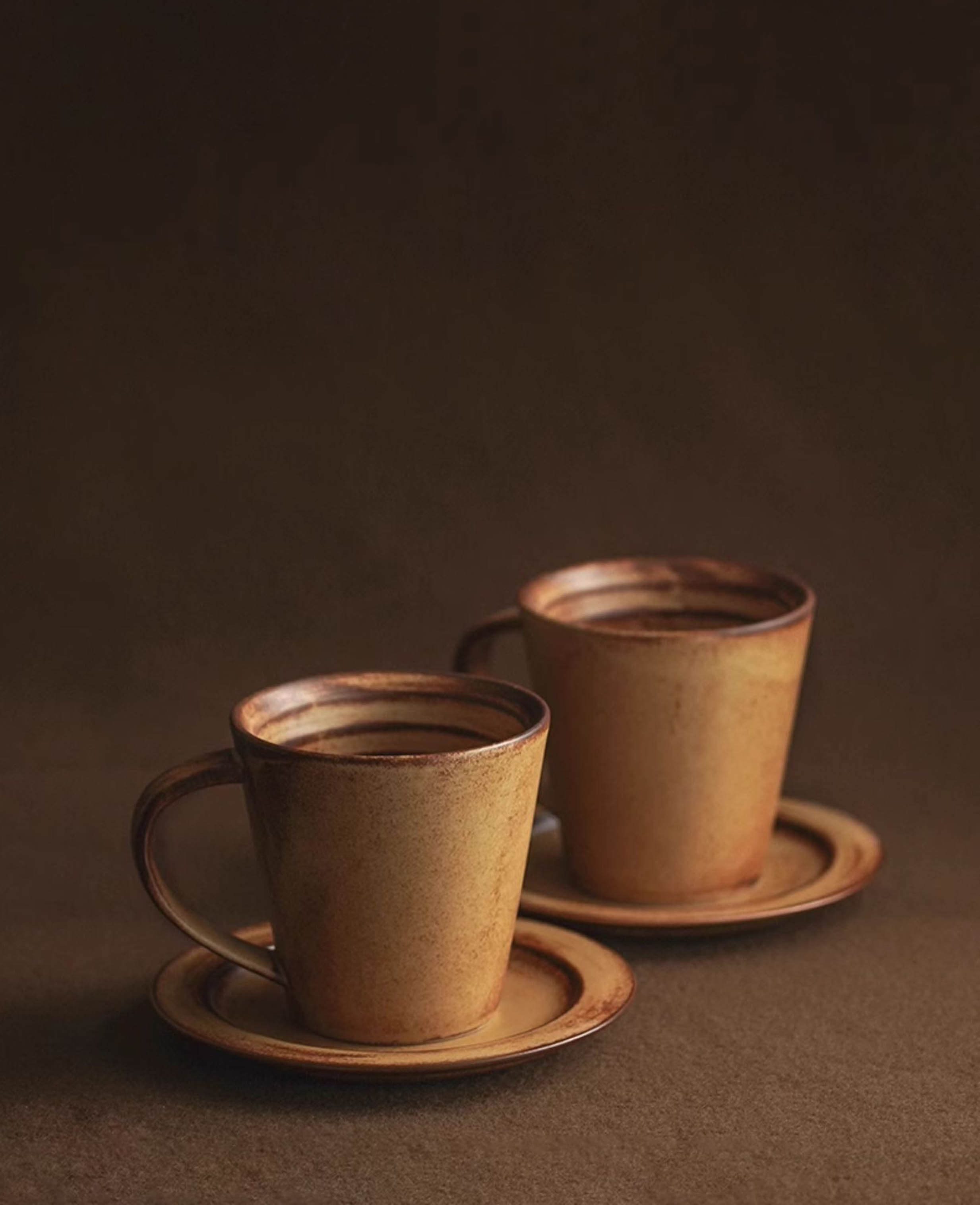 pair of rustic toffee reverie thalen coffee mugs with saucers on dark brown background