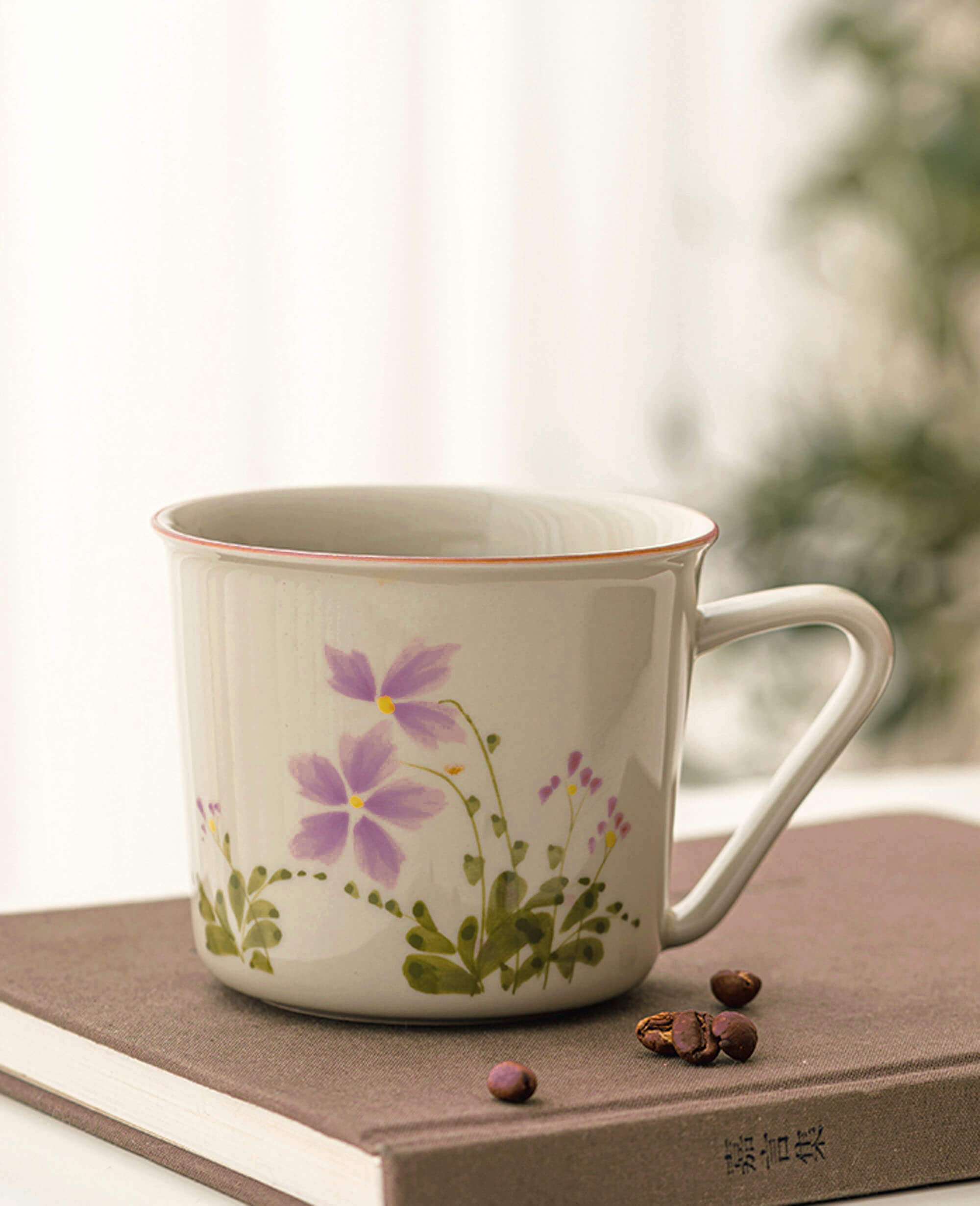 april verse porcelain cup with soft pink flowers and greenery styled with coffee beans and a book