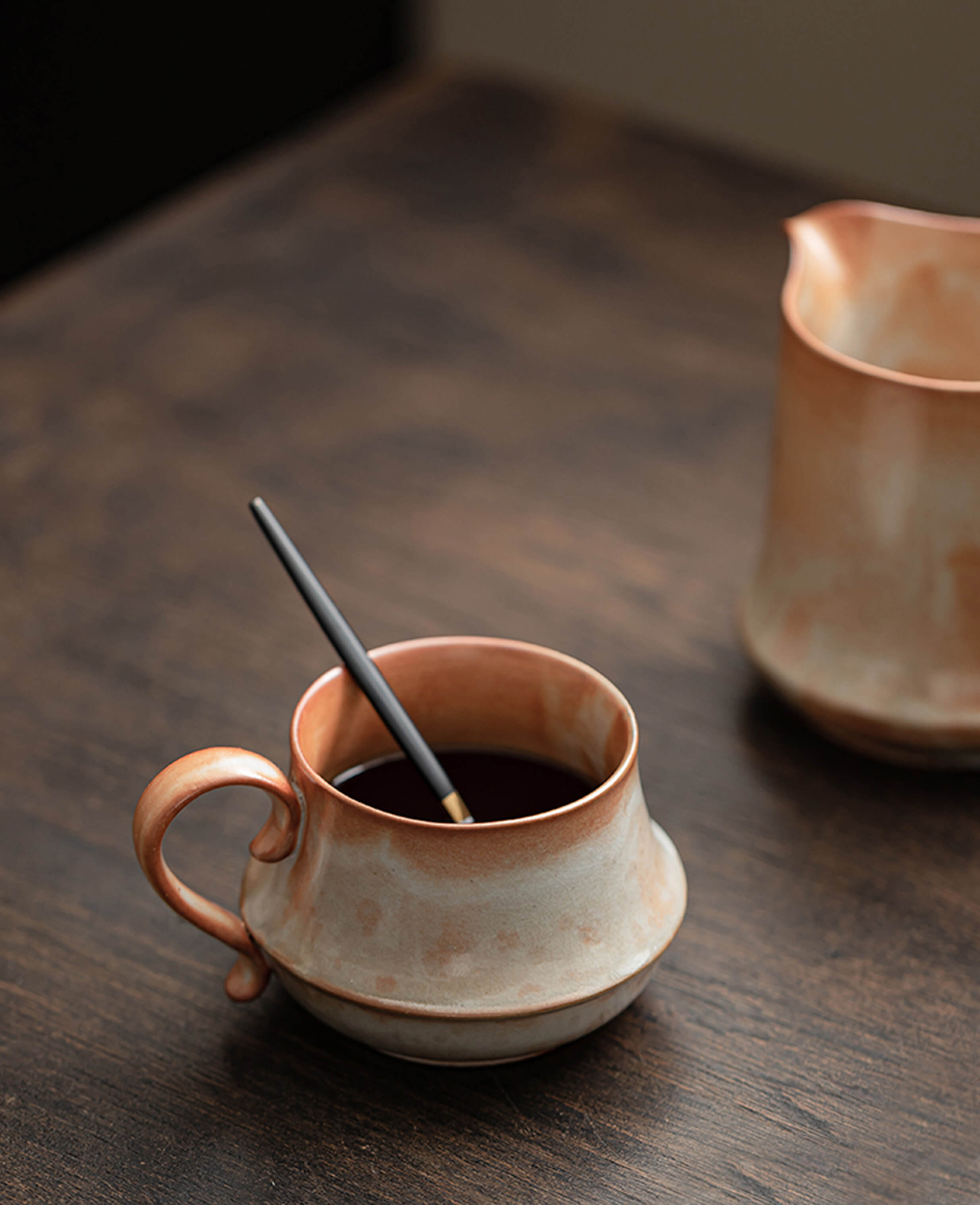 handcrafted claybourne ceramic coffee and tea cup with warm terracotta glaze placed on wooden table with pencil inside artisan stoneware