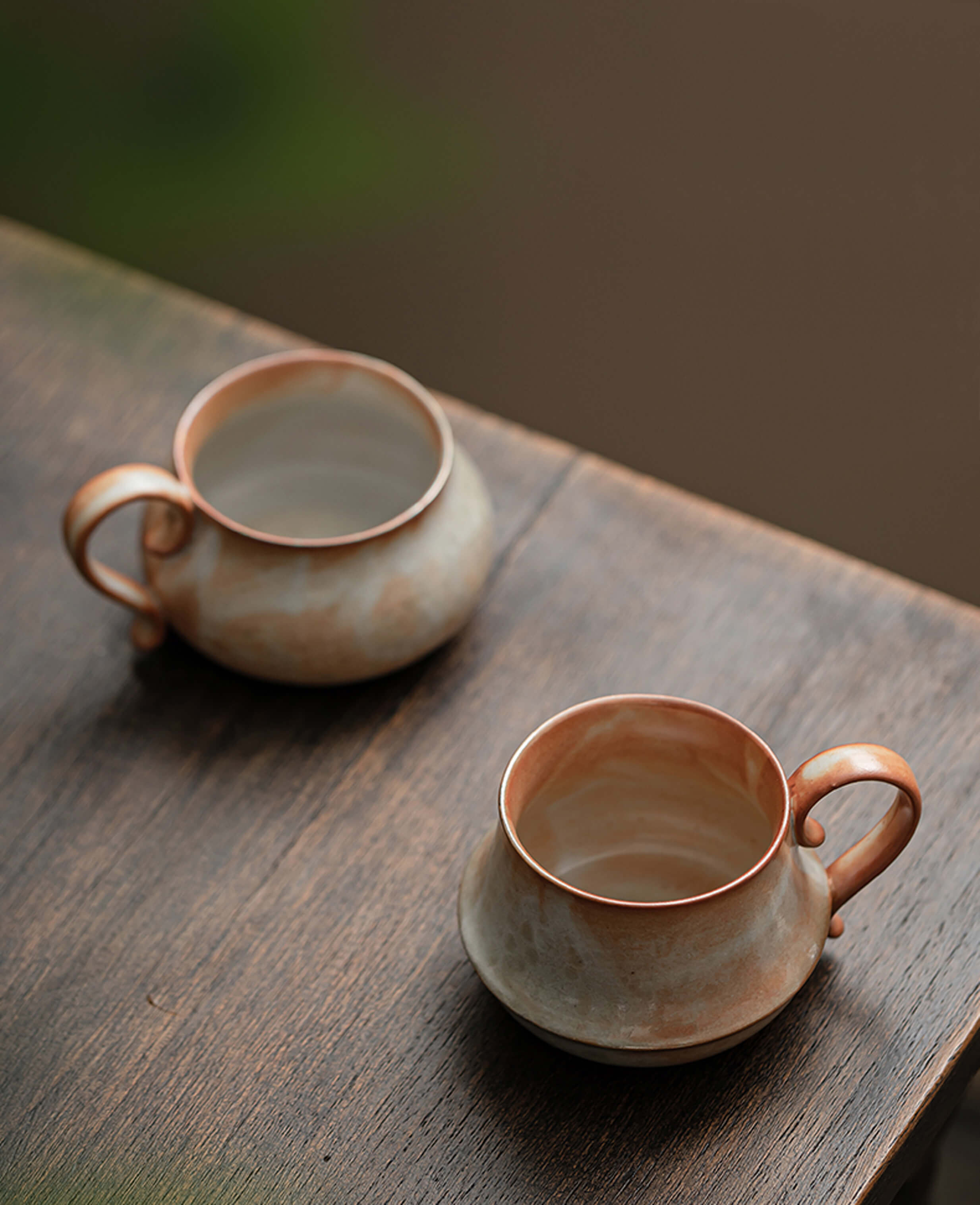 two handcrafted claybourne ceramic coffee and tea cups with warm terracotta glaze on wooden table rustic artisan stoneware