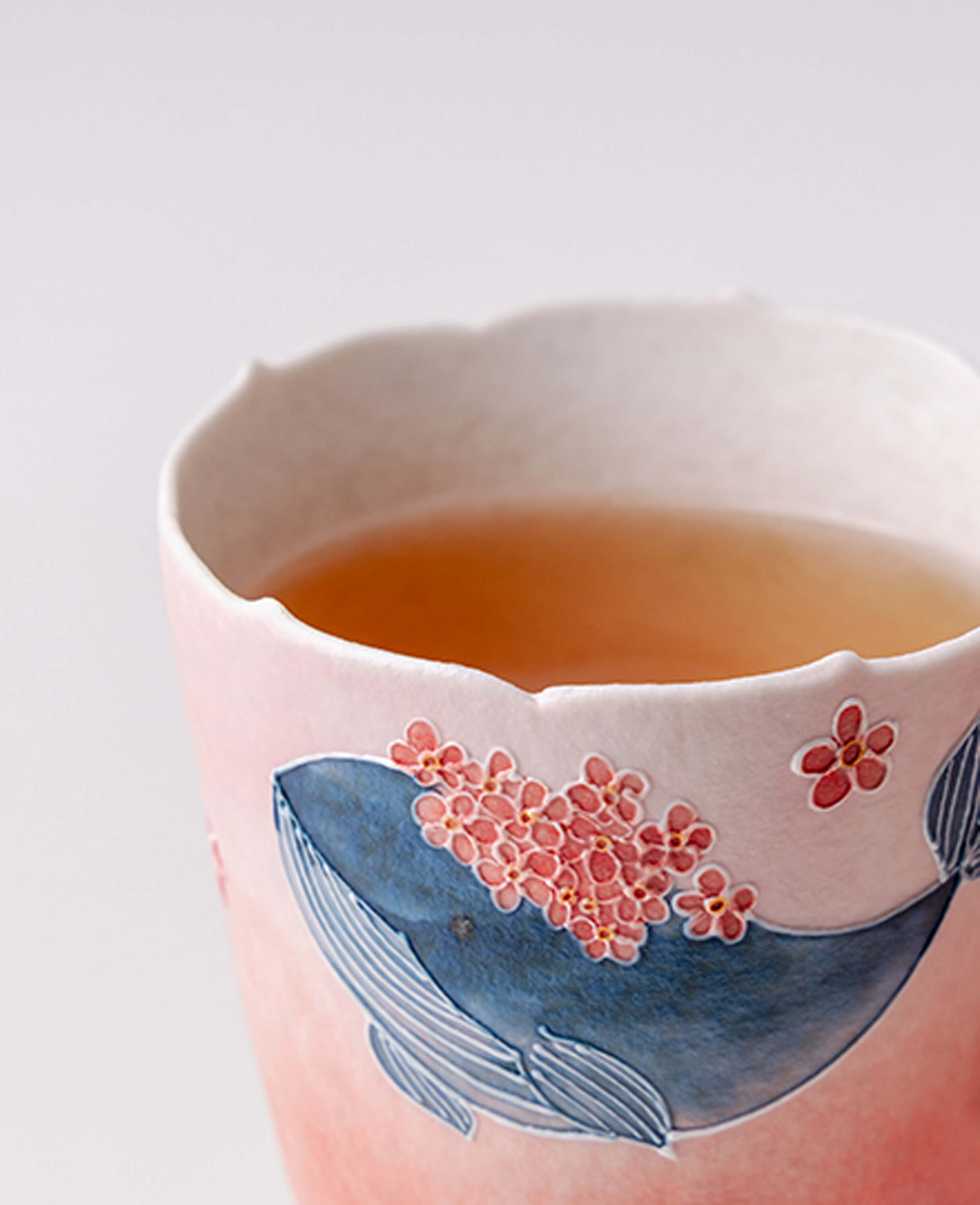 dream tide porcelain tea cup with whale and coral blossom motif filled with warm tea close up