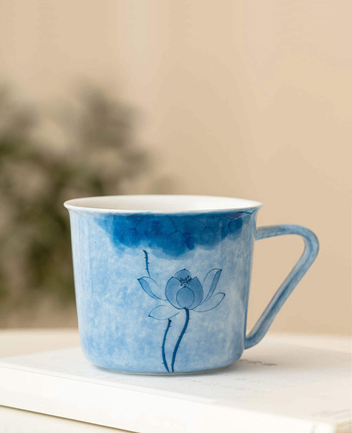 inked drizzle hand painted coffee and tea mug with blue lotus pattern sitting on book in warm natural light