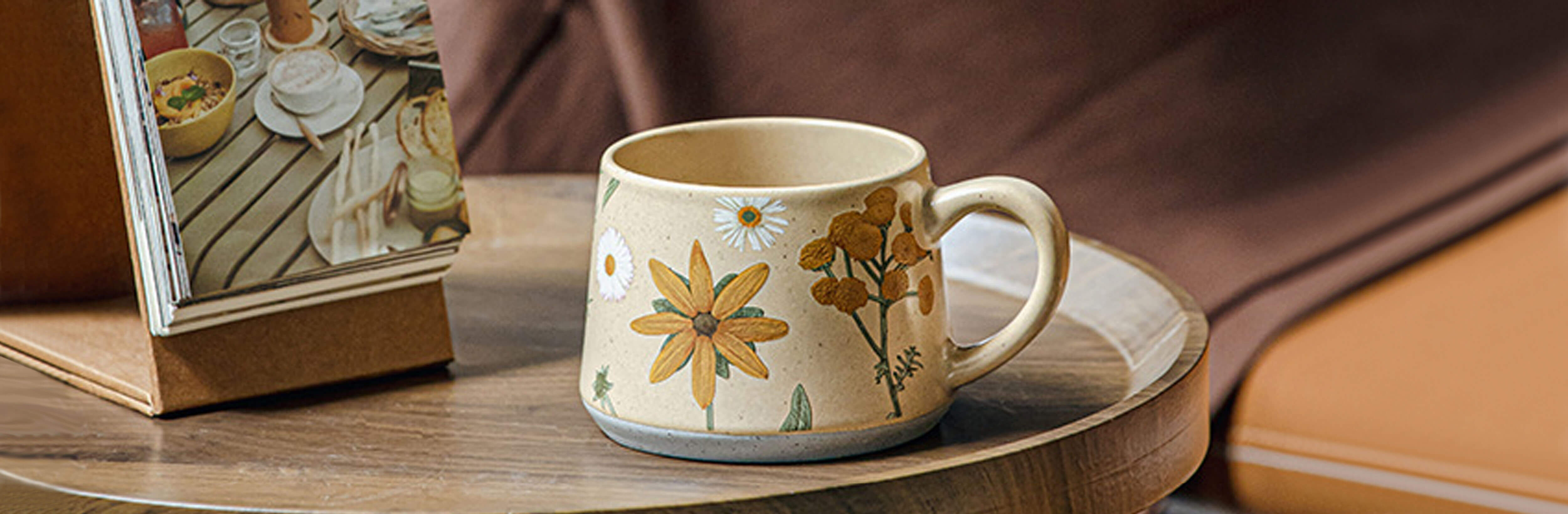 june whisper stoneware coffee and tea mug with yellow wildflower design on table home page slide image
