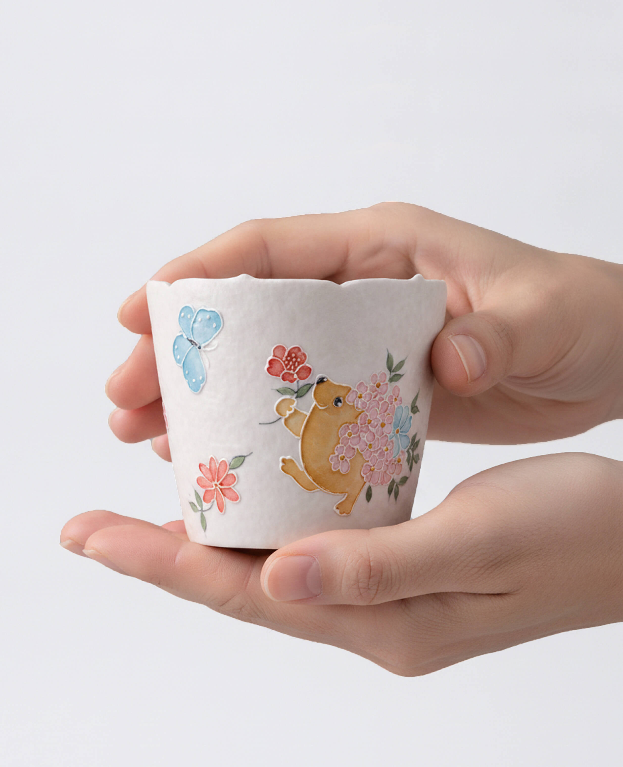 front view of kindred waltz cute handmade ceramic coffee and tea cup held in hands with whimsical floral and animal design