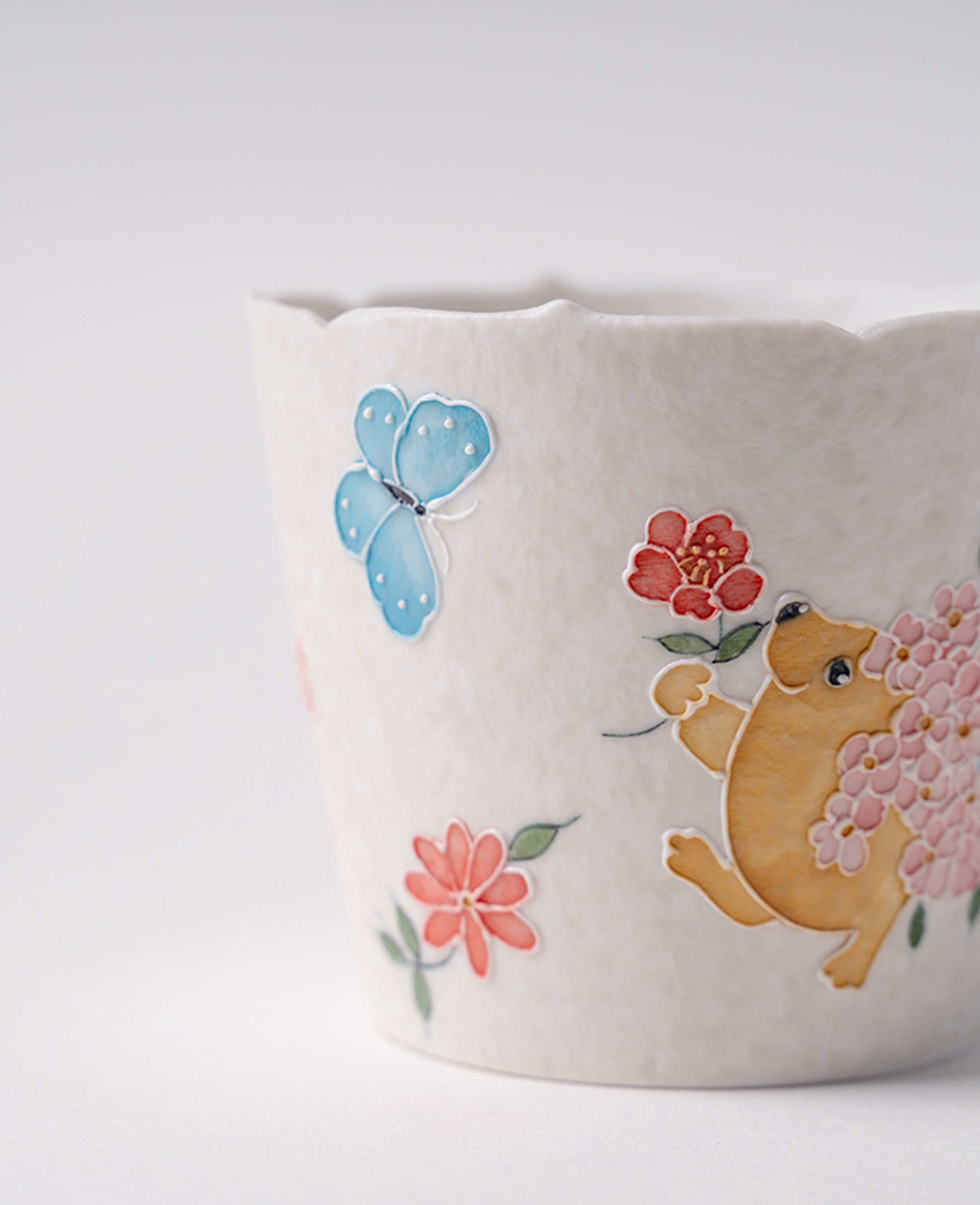 close up of kindred waltz ceramic cup showing blue butterfly red flowers and playful hedgehog in blossoms