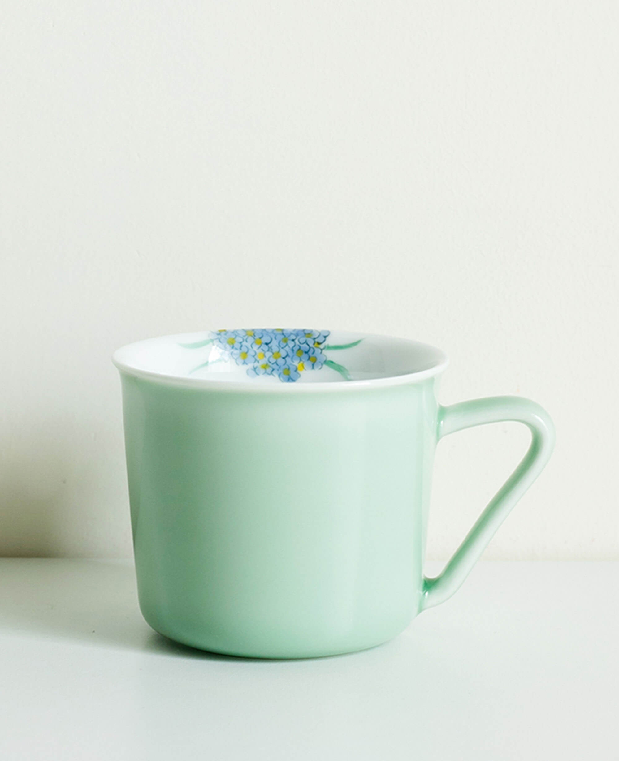 side profile of minted memory hand painted porcelain cup with floral motif resting on a white surface