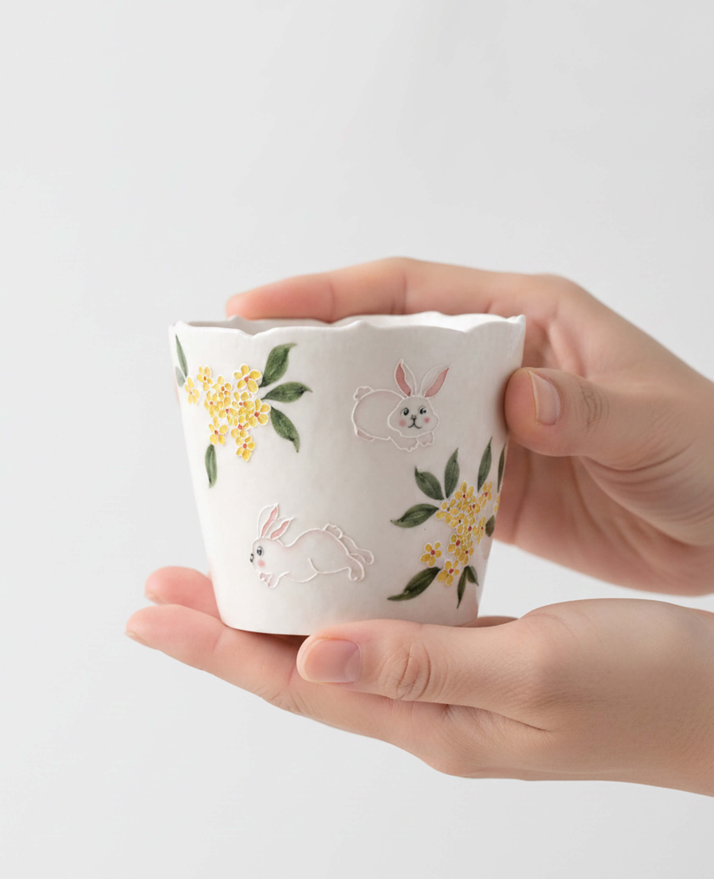 nectar hop hand painted ceramic coffee and tea cup with rabbit and osmanthus flower design held in hands for display 