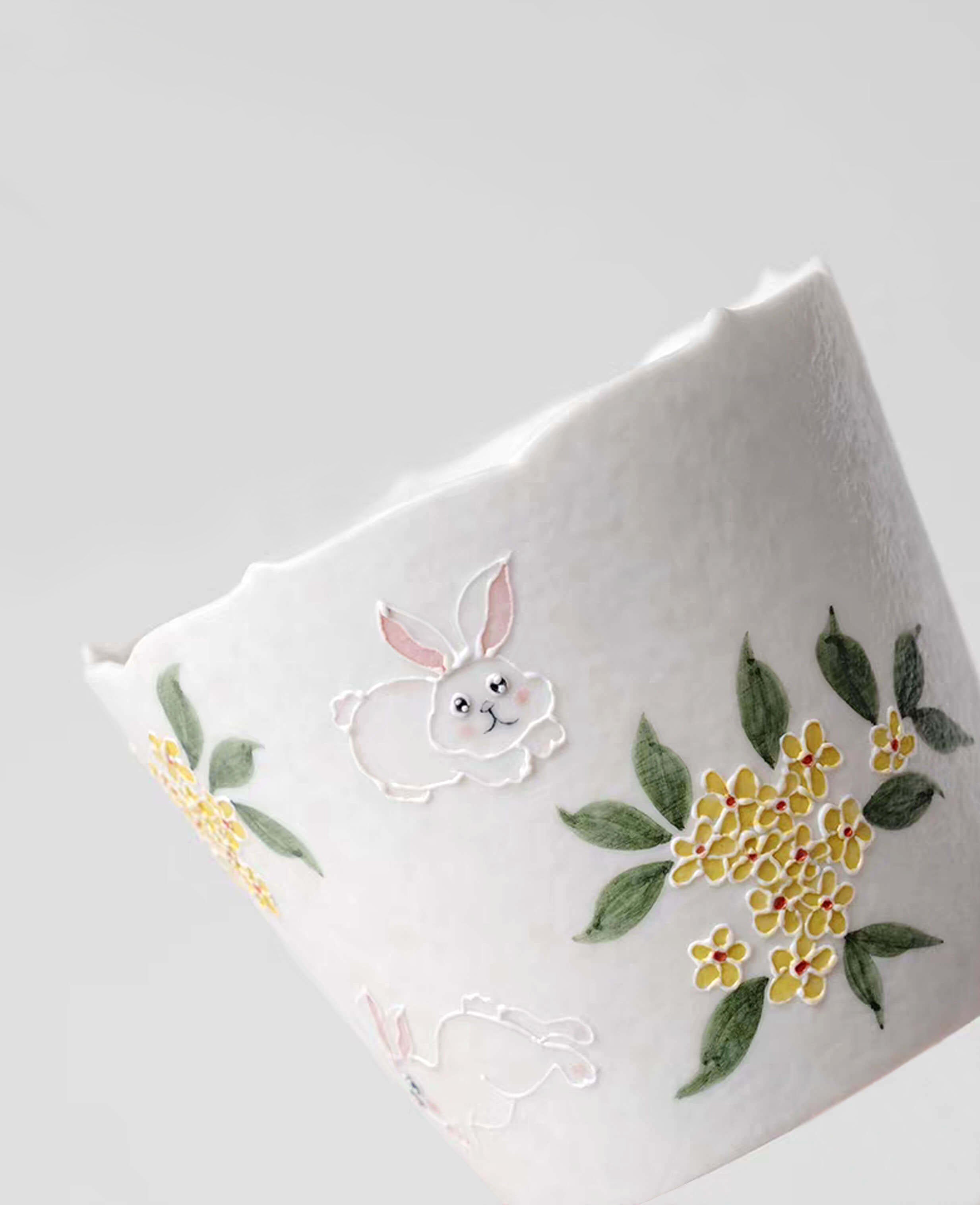 close up of nectar hop hand painted ceramic cup showing rabbit leaping among golden osmanthus blossoms angled view