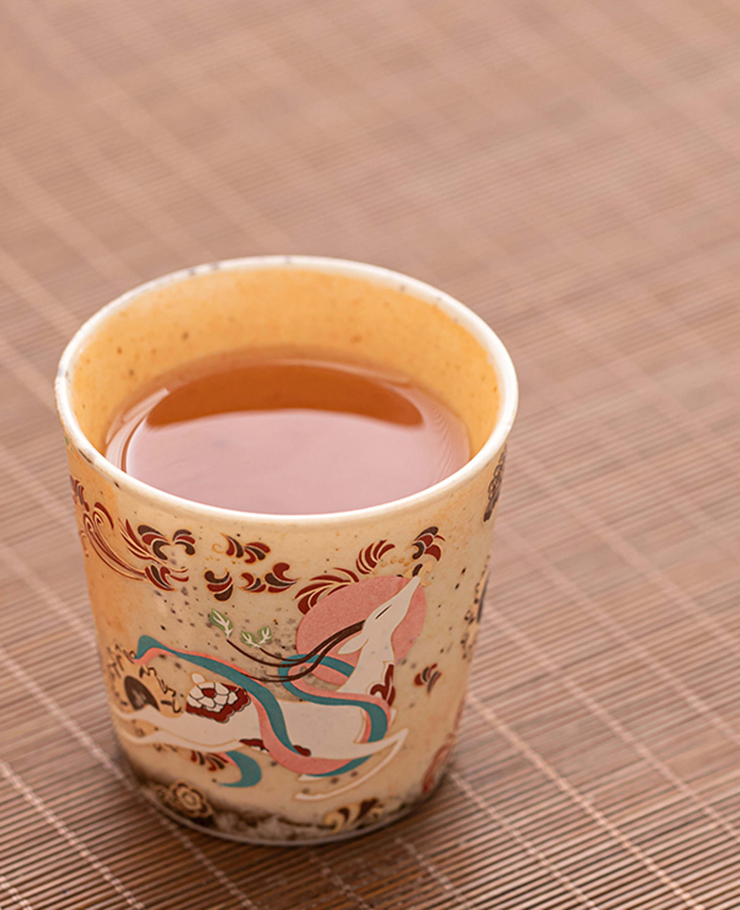 close-up of warm tea served in a hand-glazed ceramic espresso cup featuring a mythical motif