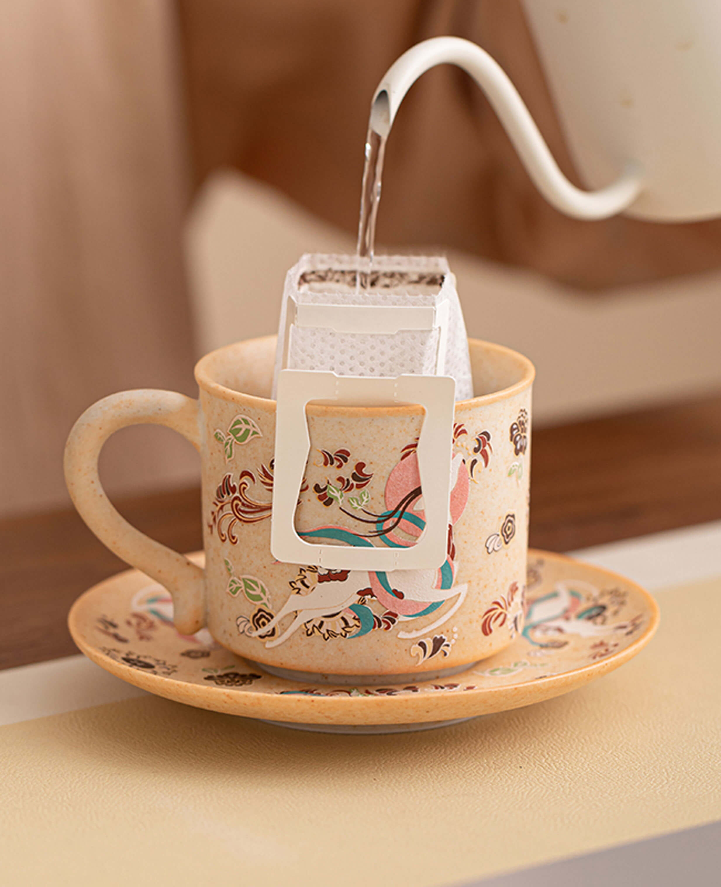 hot water being poured into filter bag in nine coloured deer ceramic mug with saucer