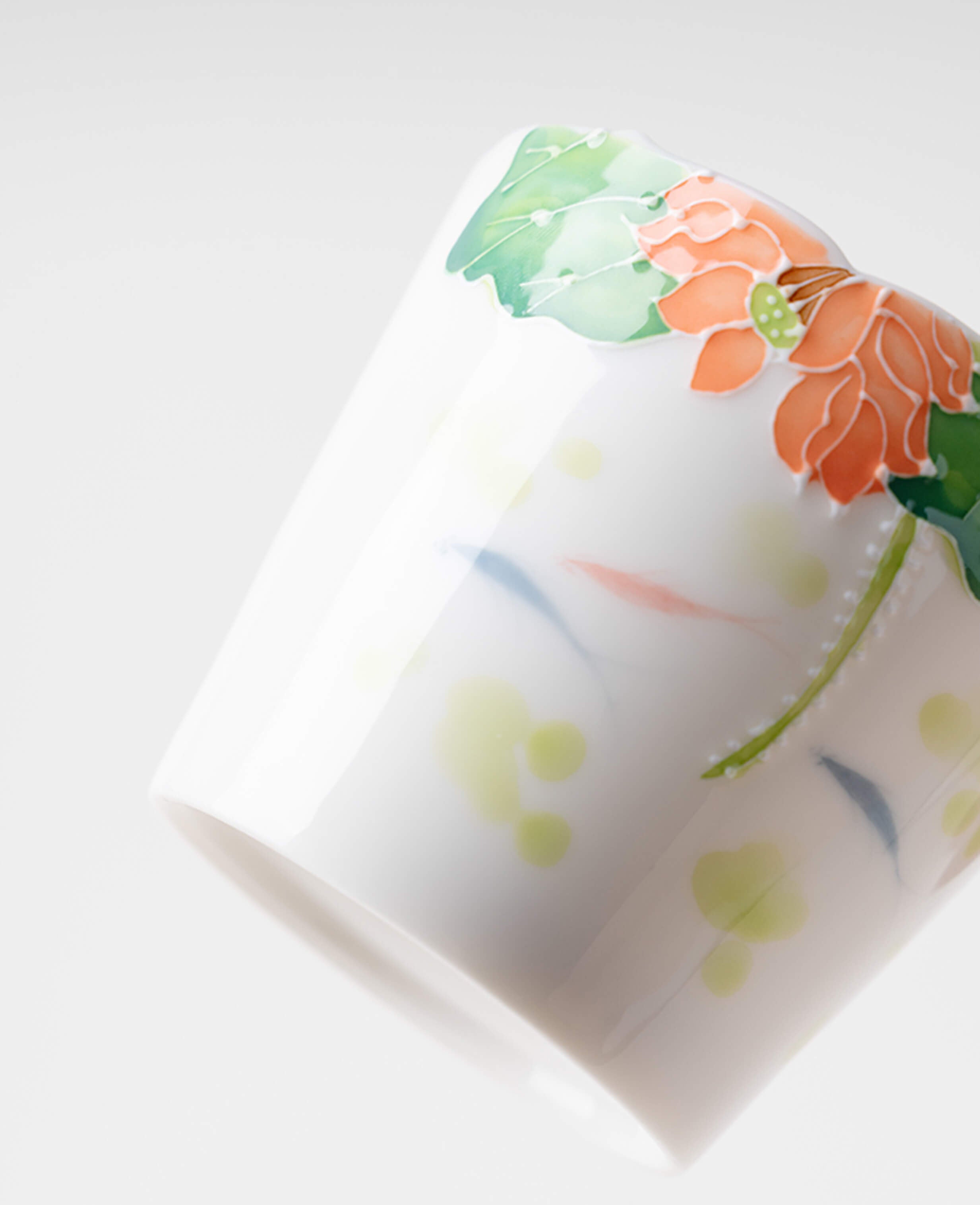 hand painted porcelain coffee and tea cup with lotus flower and green leaf detail photographed at an angle on white background