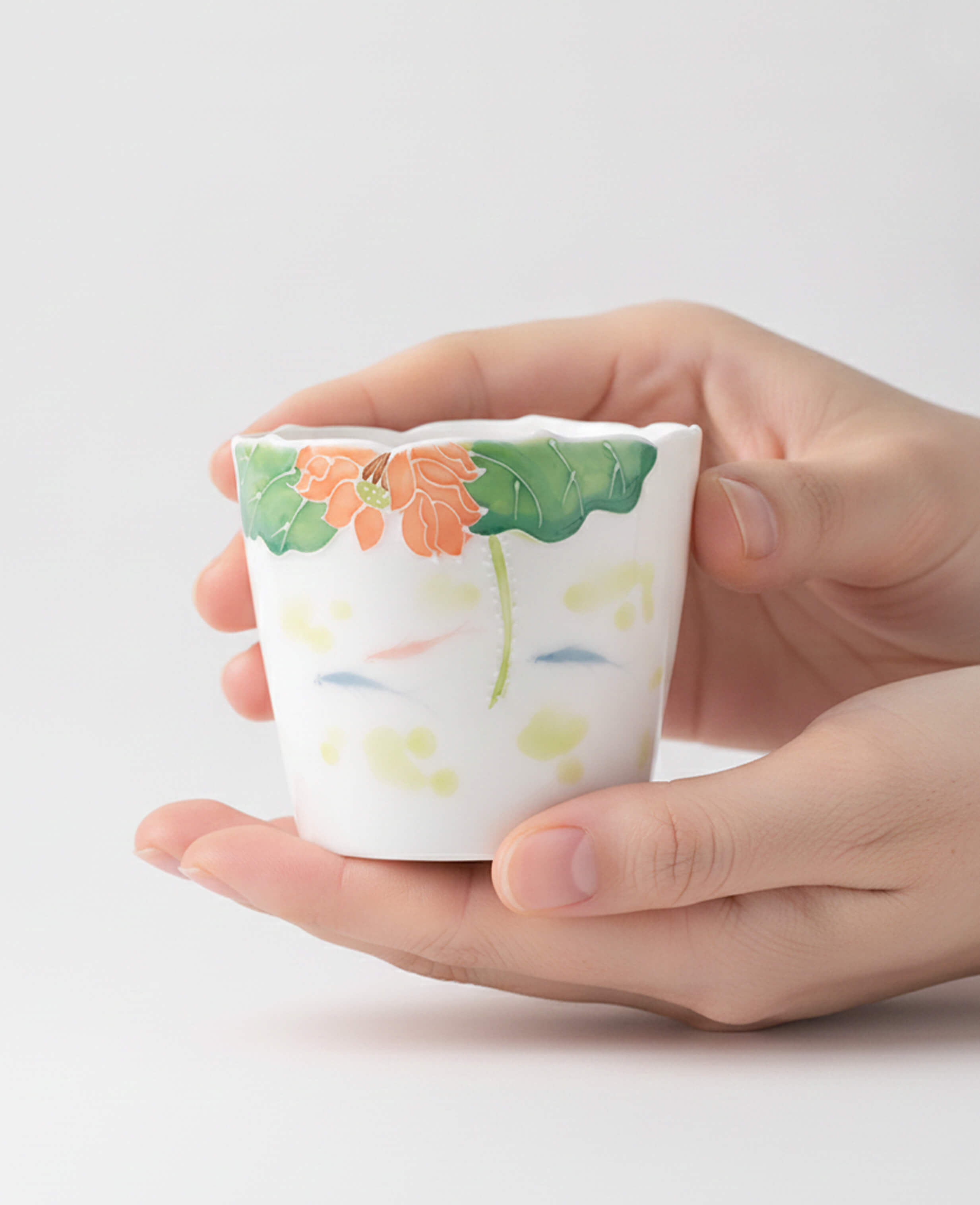 handcrafted porcelain coffee and tea cup decorated with lotus flower and water motif held in hands for display