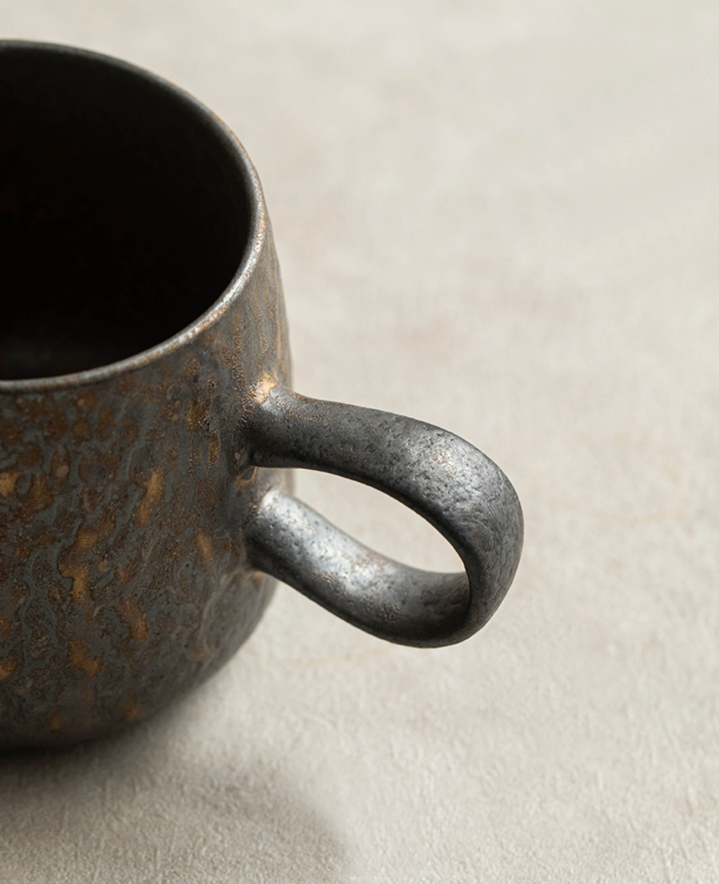 a close-up of the curved handle on the handcrafted ceramic rustglow lumen coffee cup, showcasing its rustic glaze and textured finish