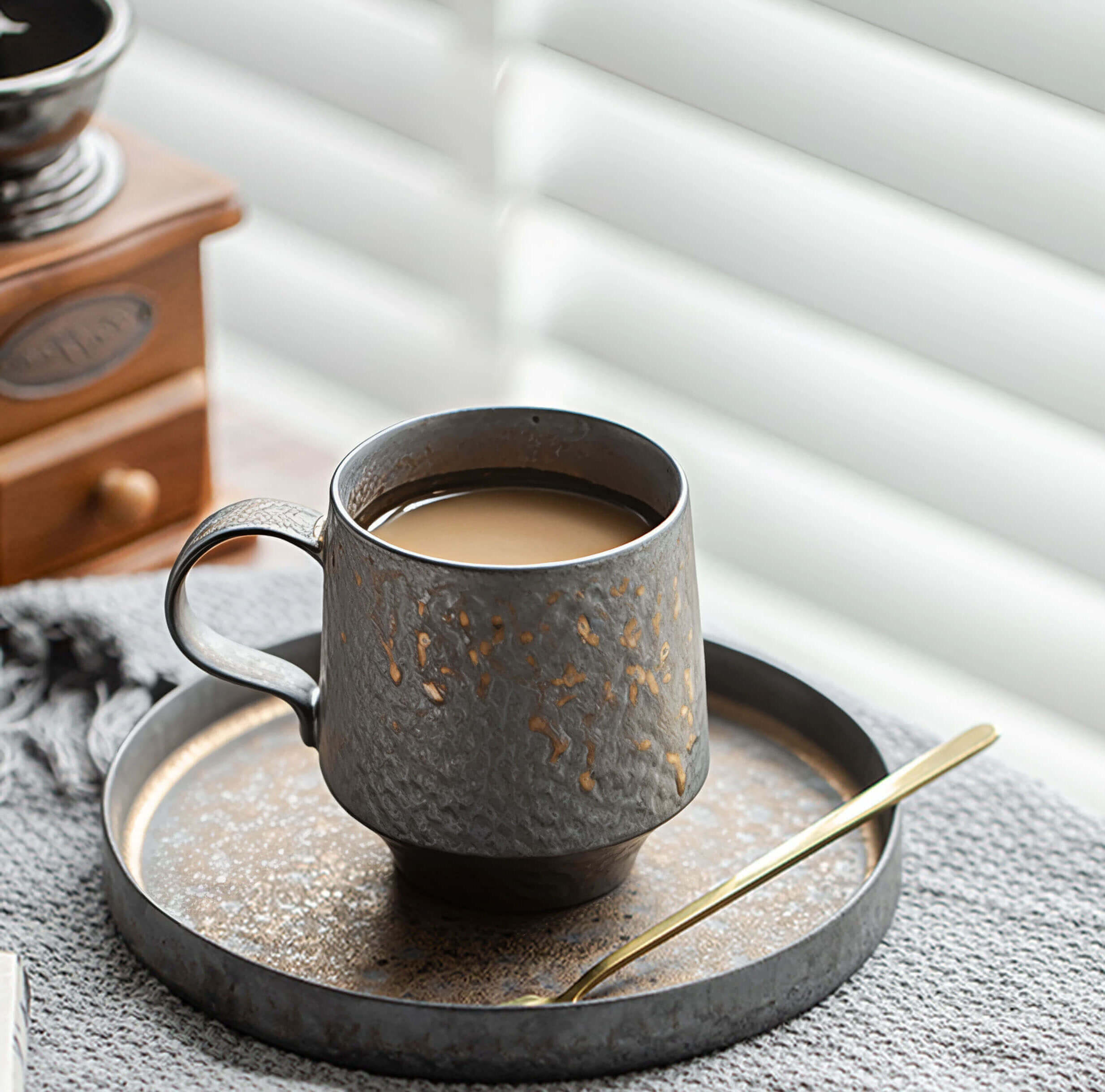 textured ceramic coffee cup in deep rust tones with saucer and gold spoon bathed in morning light beside a window