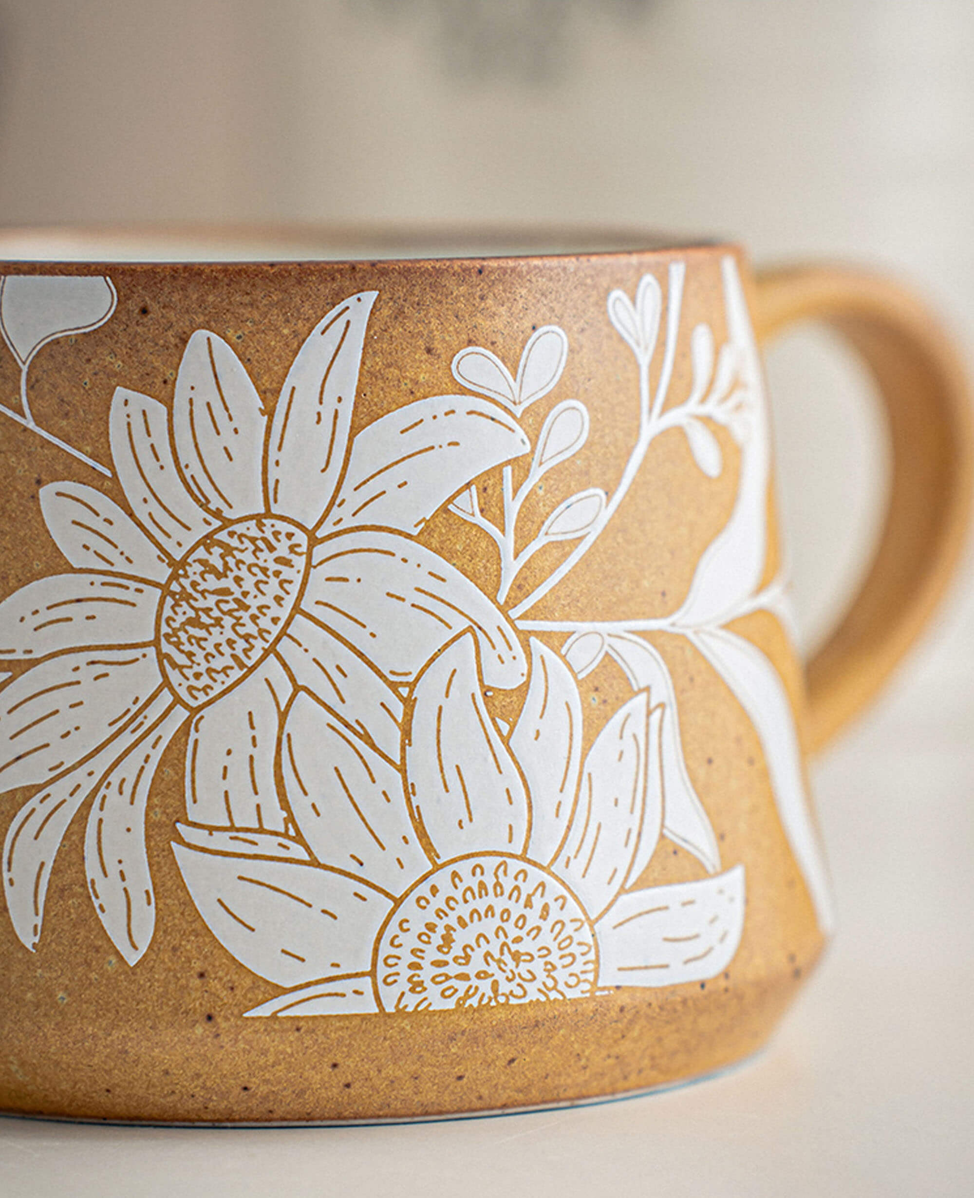 close up of ochre ceramic mug showing intricate white floral pattern and engraved botanical details