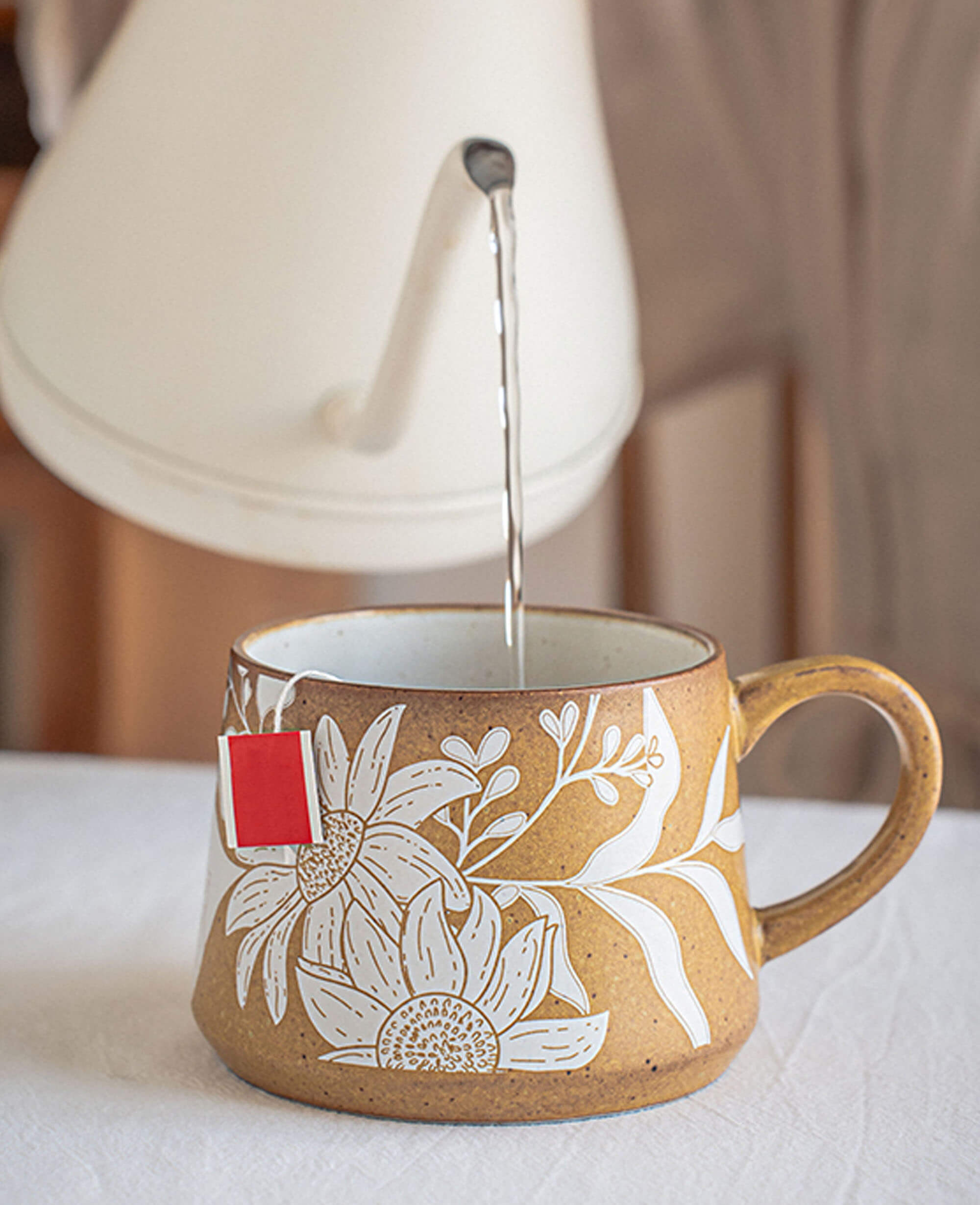 rustic ochre ceramic mug with white etched floral design hot tea being poured from white kettle