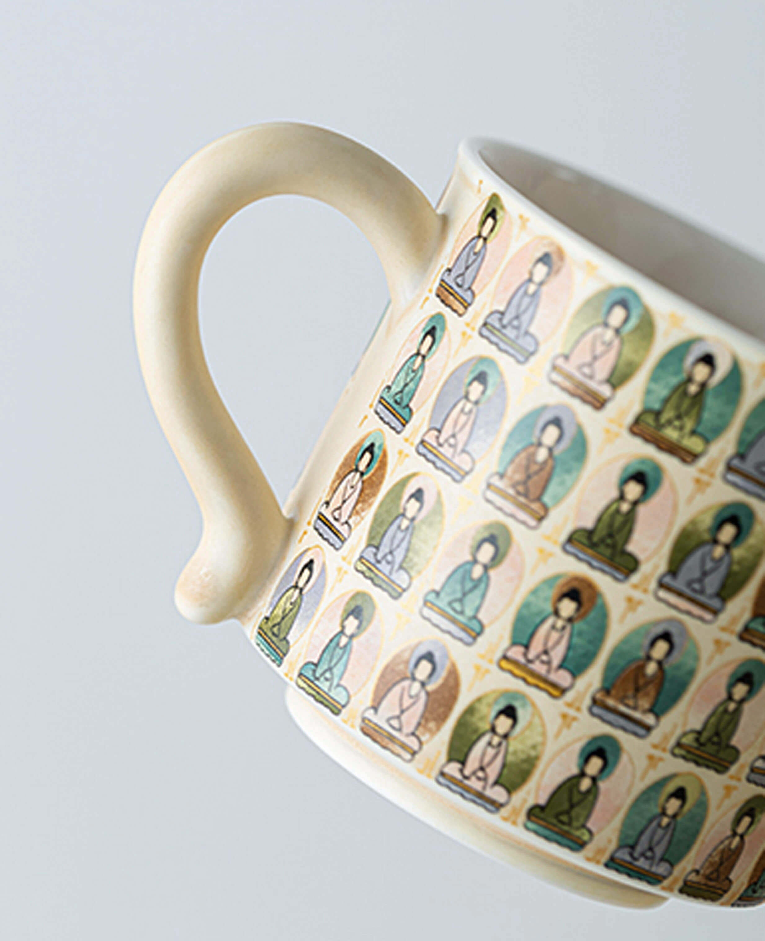 closeup of ceramic cup handle showing colourful miniature buddha illustrations in traditional style