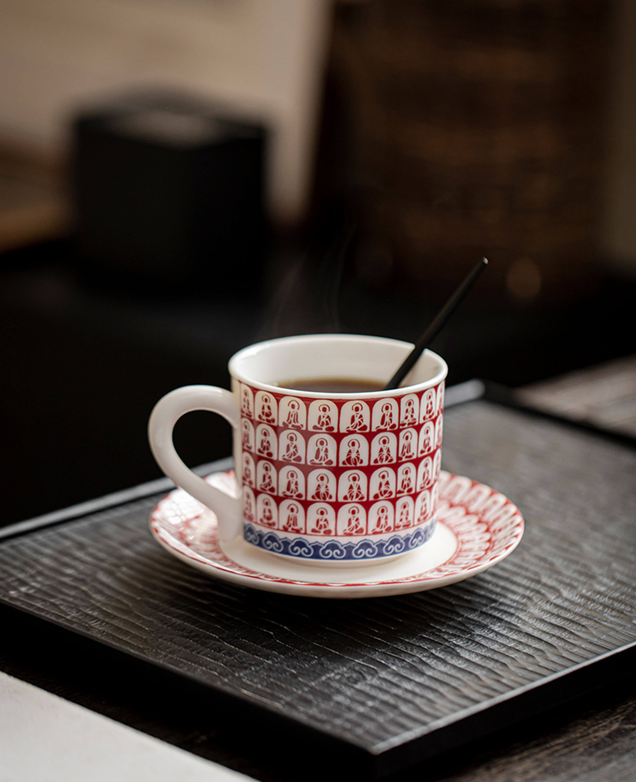 steaming coffee inside red thousand buddhas ceramic coffee cup on textured black tray