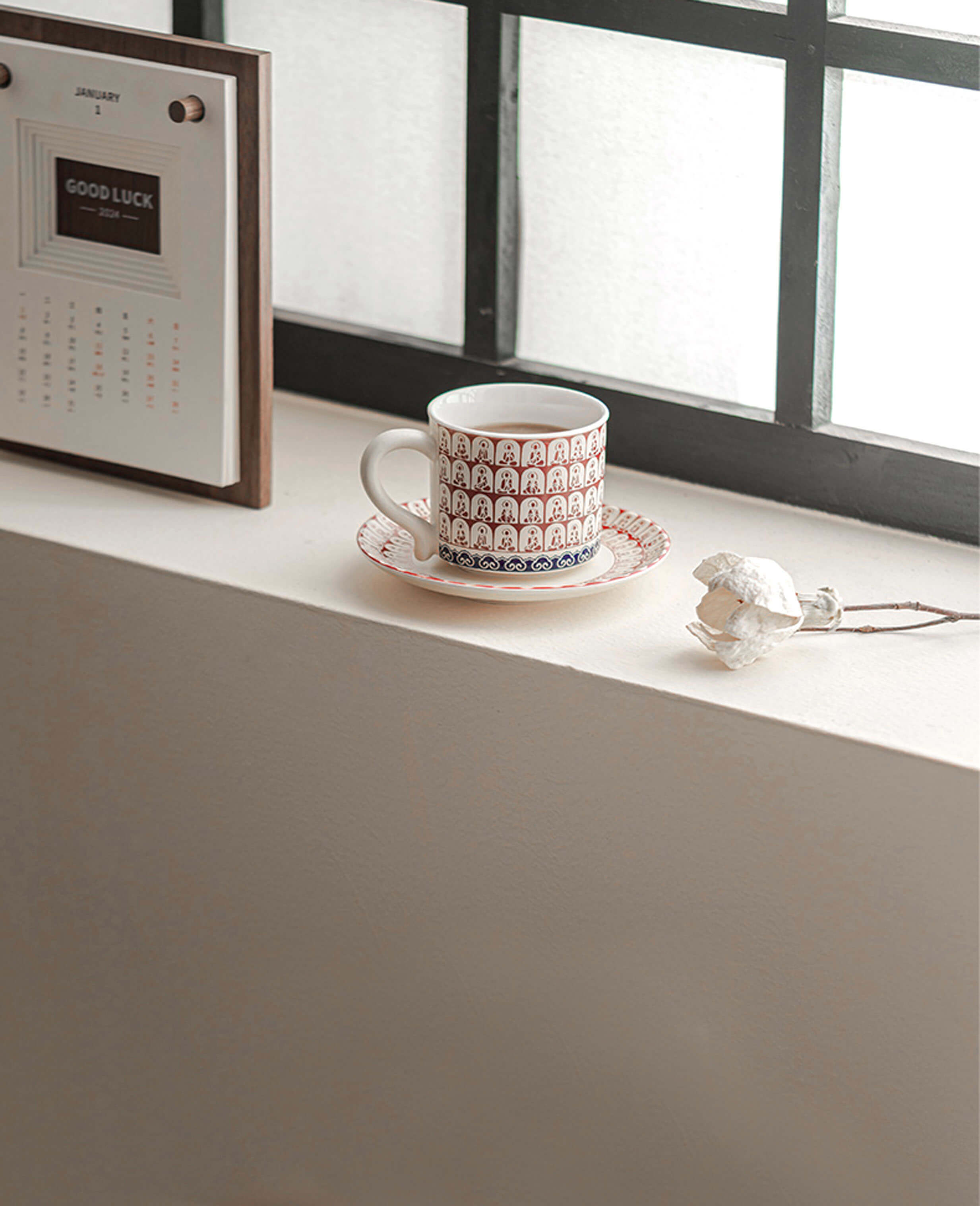 thousand buddhas crimson ceramic coffee cup and saucer placed by window with dried rose flower