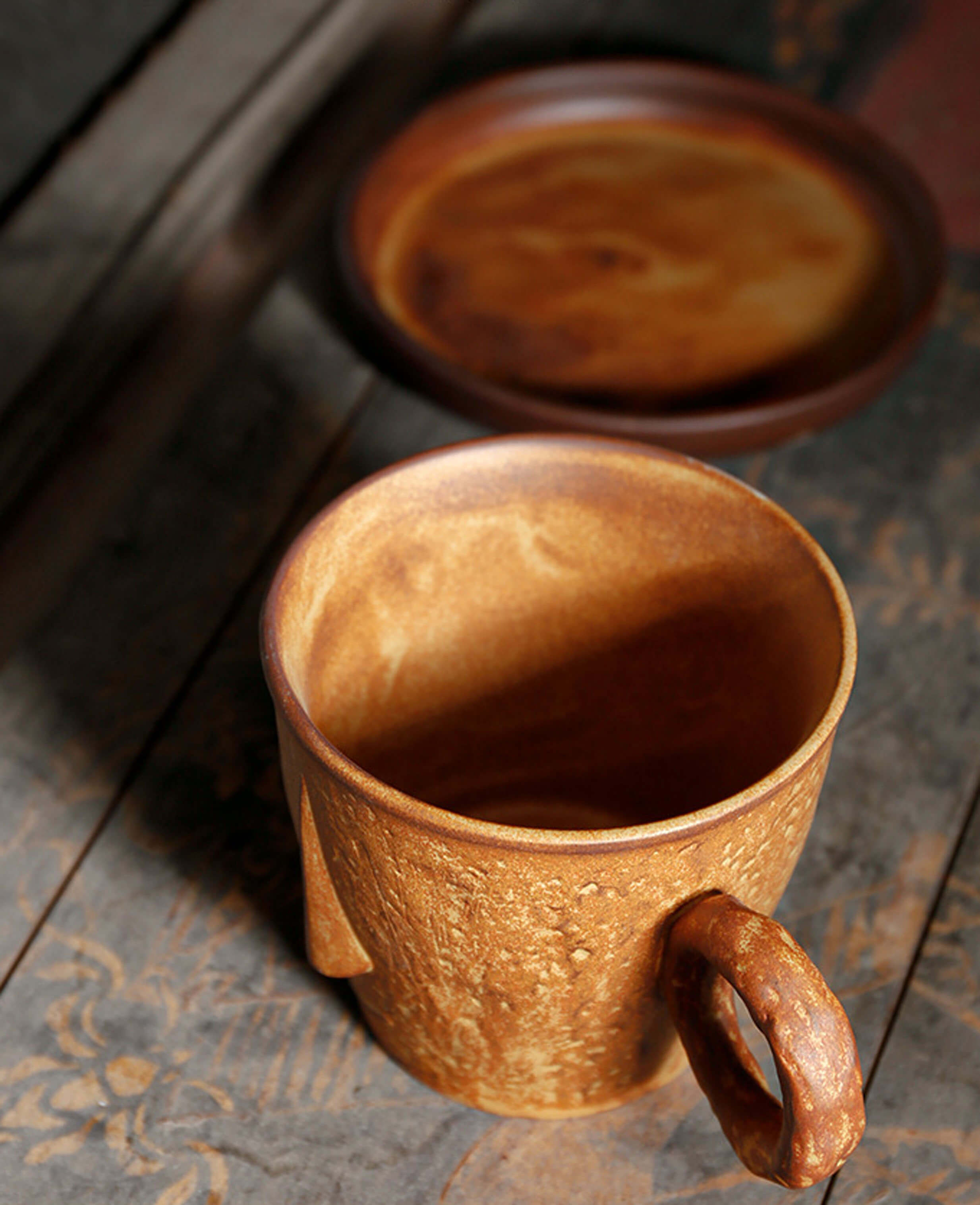 overhead view of toffee reverie muse ceramic coffee mug showing interior glaze and matching saucer in the background on a rustic wooden table