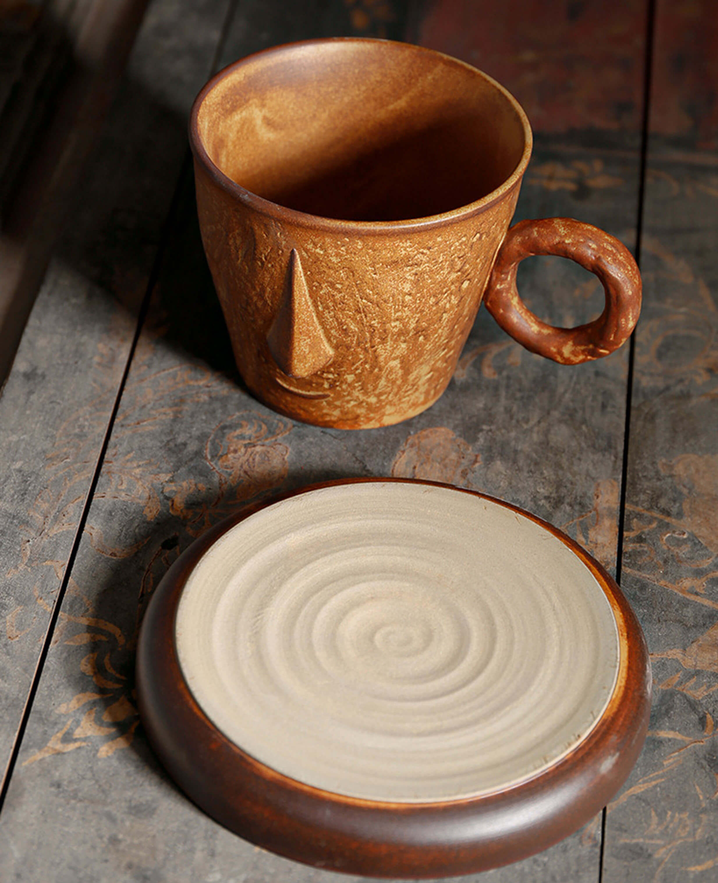 top-down view of toffee reverie muse mug and saucer with unglazed spiral base on a textured wooden table