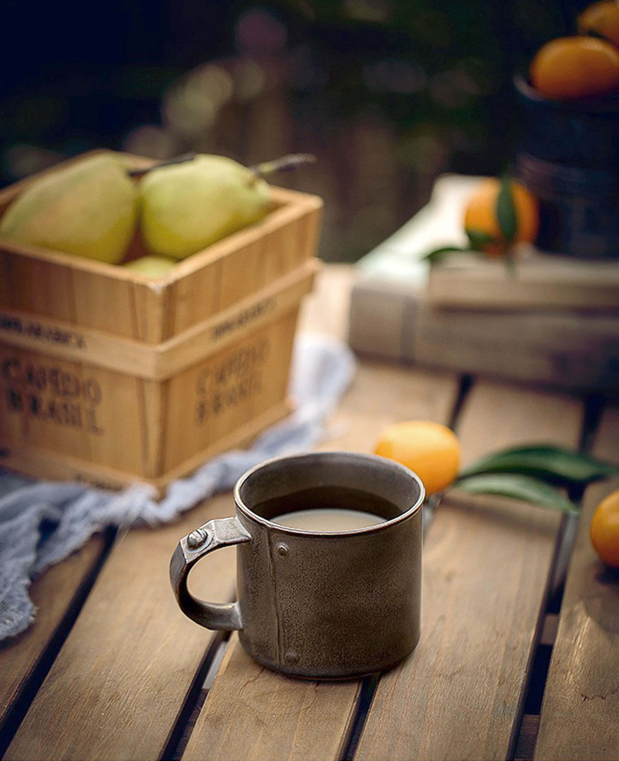 rustic handmade ceramic coffee mug with milk on wooden table beside fruits