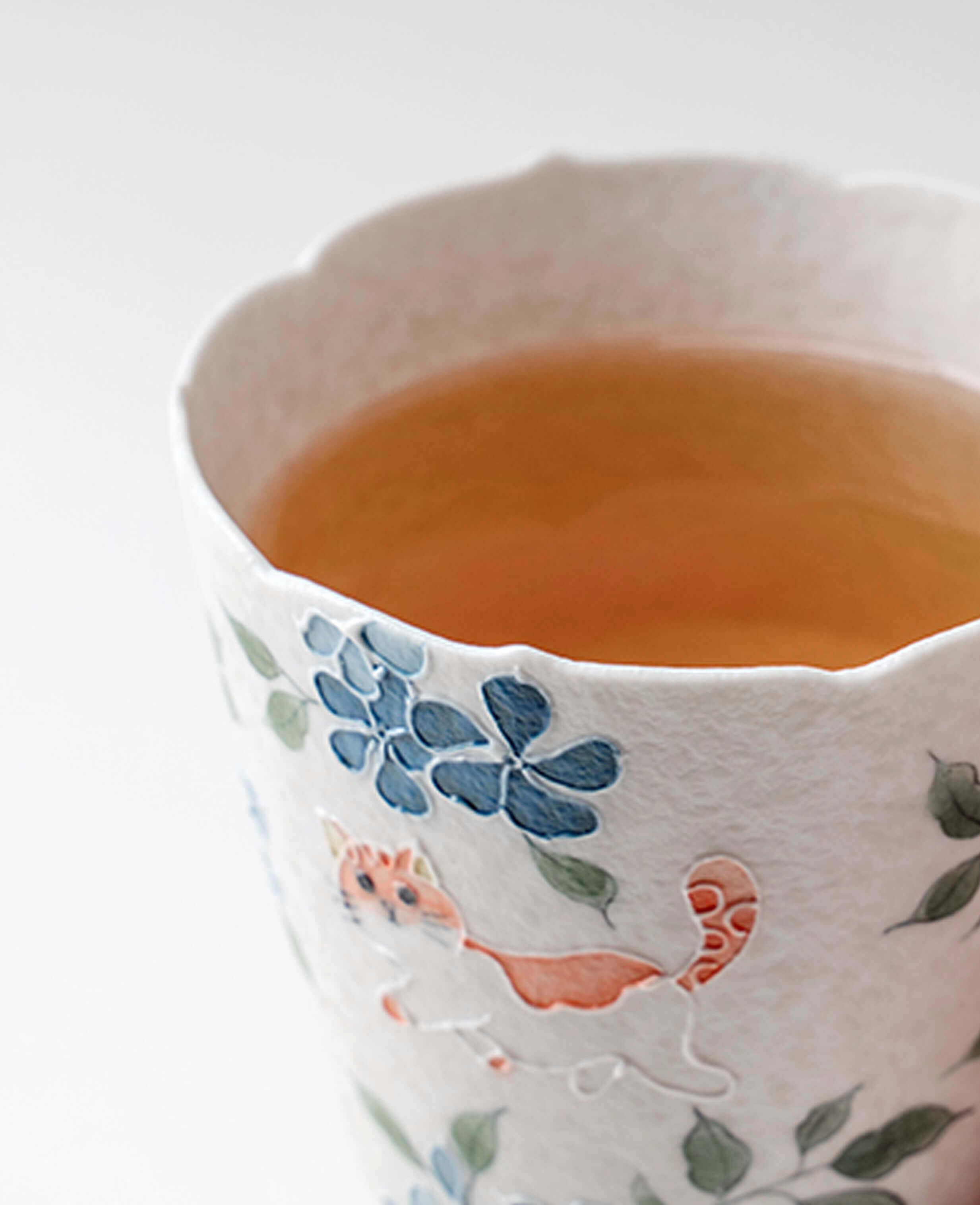 whisker trail handcrafted porcelain cup close up with orange cat motif and warm tea inside